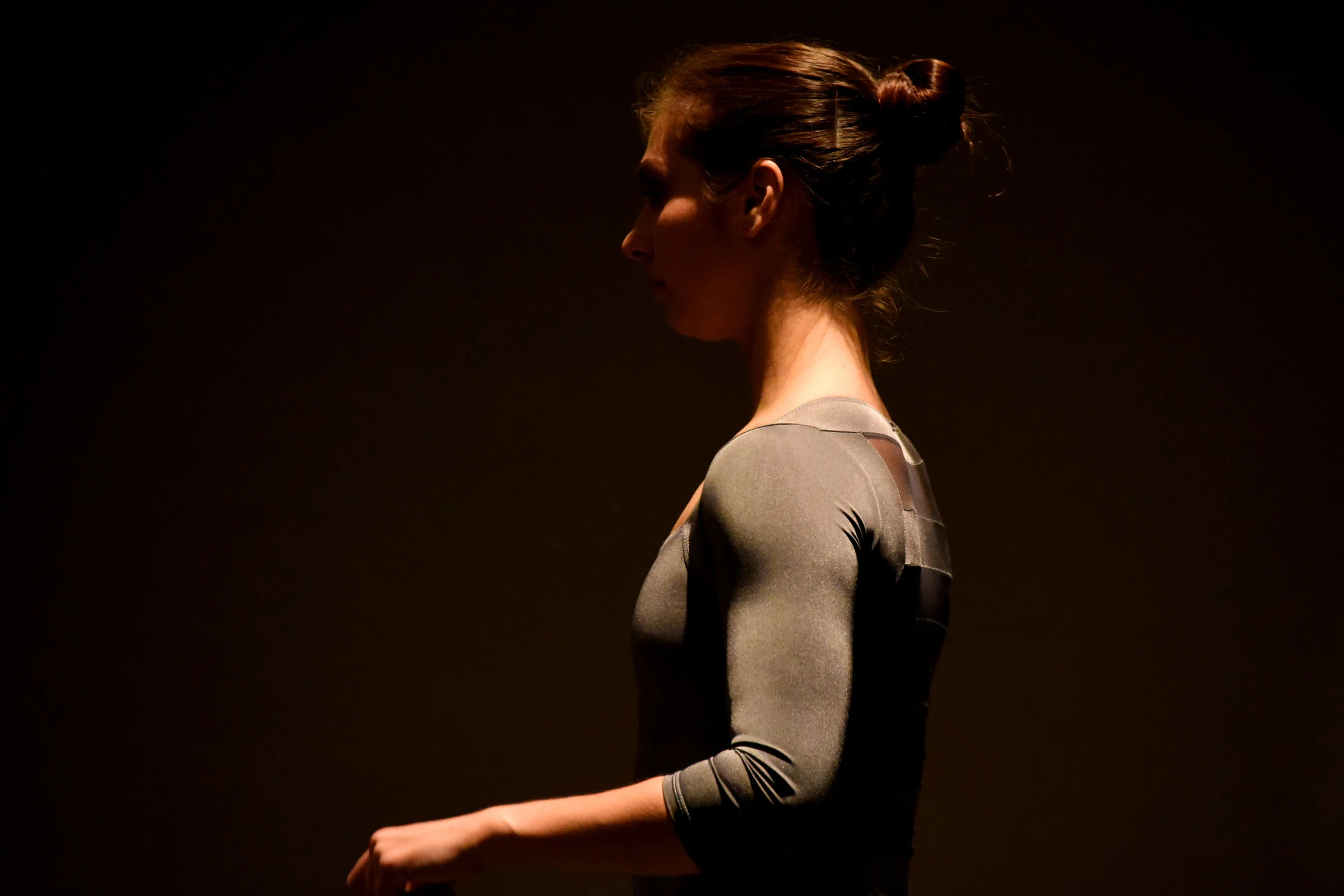 Close up of dancer Meagan Kolakowski warming up in costume on a dimly lit stage.