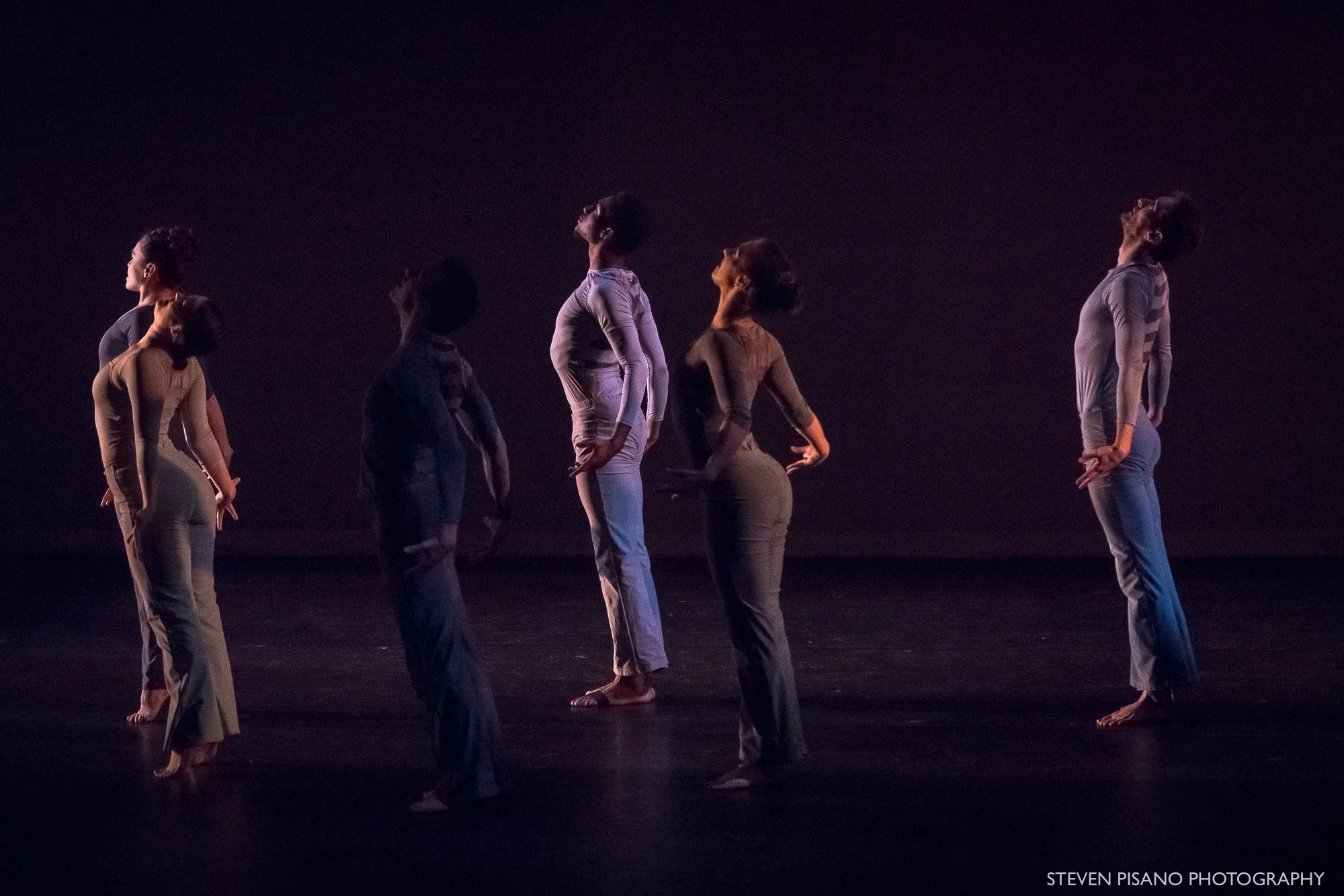 Grey. Six female and male dancers are standing on their toes and facing to the side arching their baks and looking up.