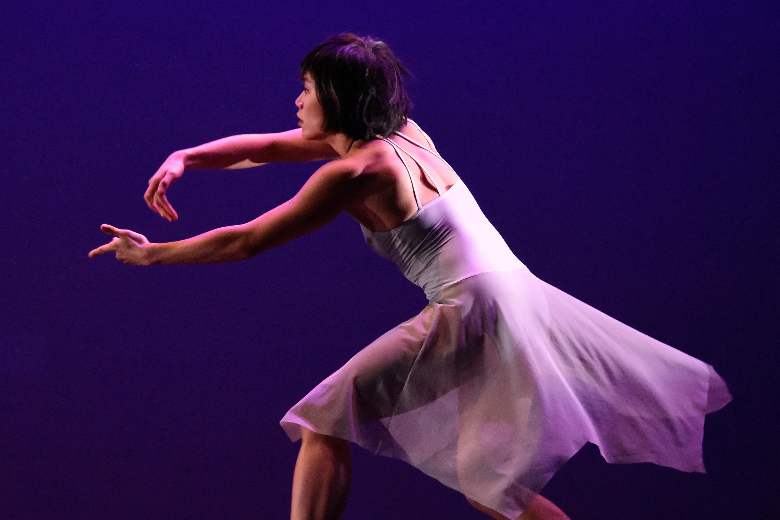 Grey. Dancer Tina Wang bends her knees and reaches both arms as she does a turn.