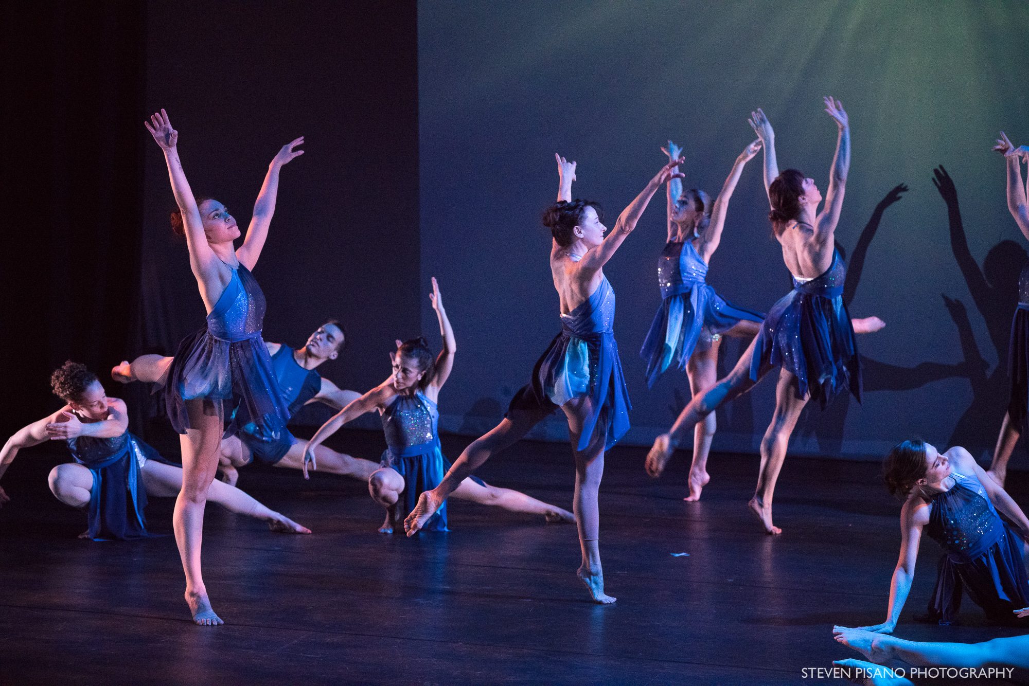 Silver Staircase. Against a backdrop that has an image projected of being under water, eight male and female dancers are in various streamlined poses and movements creating a ripple effect.
