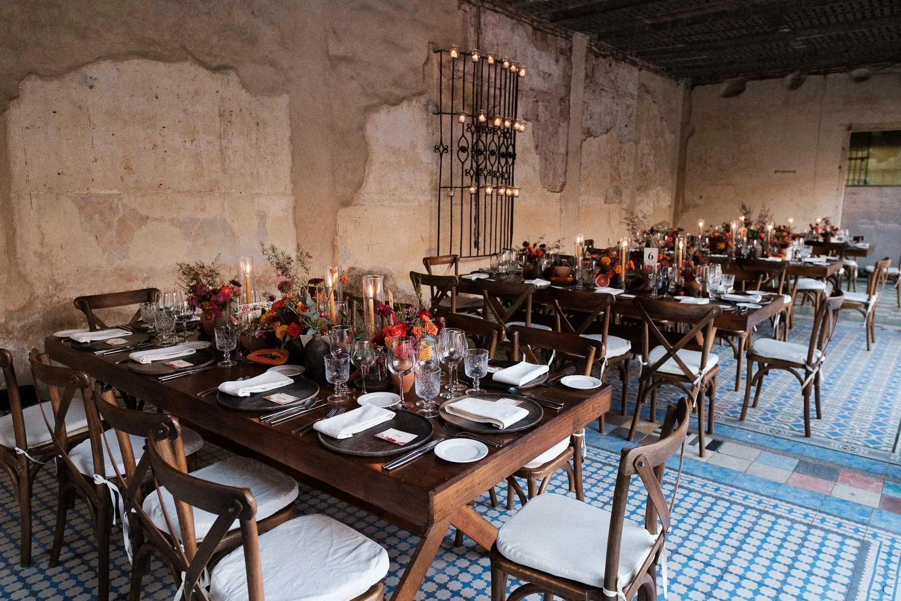 Elegant wedding reception tables with curated floral centerpieces and sophisticated place settings inside the historic ruins of Proyecto Murguia, Oaxaca, before the guests arrive.