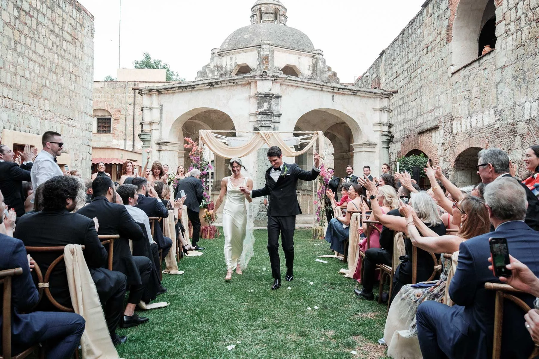 A newly married couple exits their ceremony with pure joy as family cheers, featuring the iconic historic Lavaderos as a dramatic architectural backdrop.