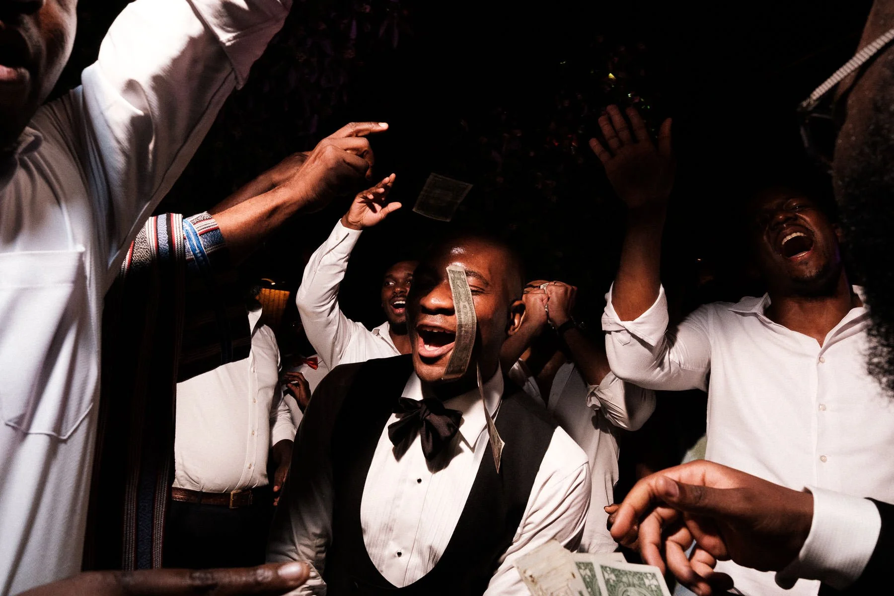 The groom performs a traditional African dance at La Fabrica Patio while guests throw dollar bills for prosperity and luck.