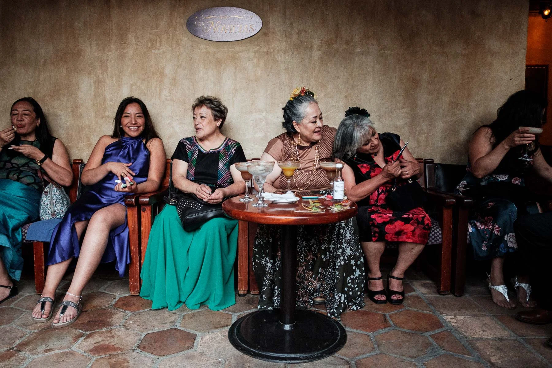 A group of elegant women captured in a street photography style during the cocktail hour at Quinta Real Oaxaca, featuring composition layers against a clean, historic architectural background.