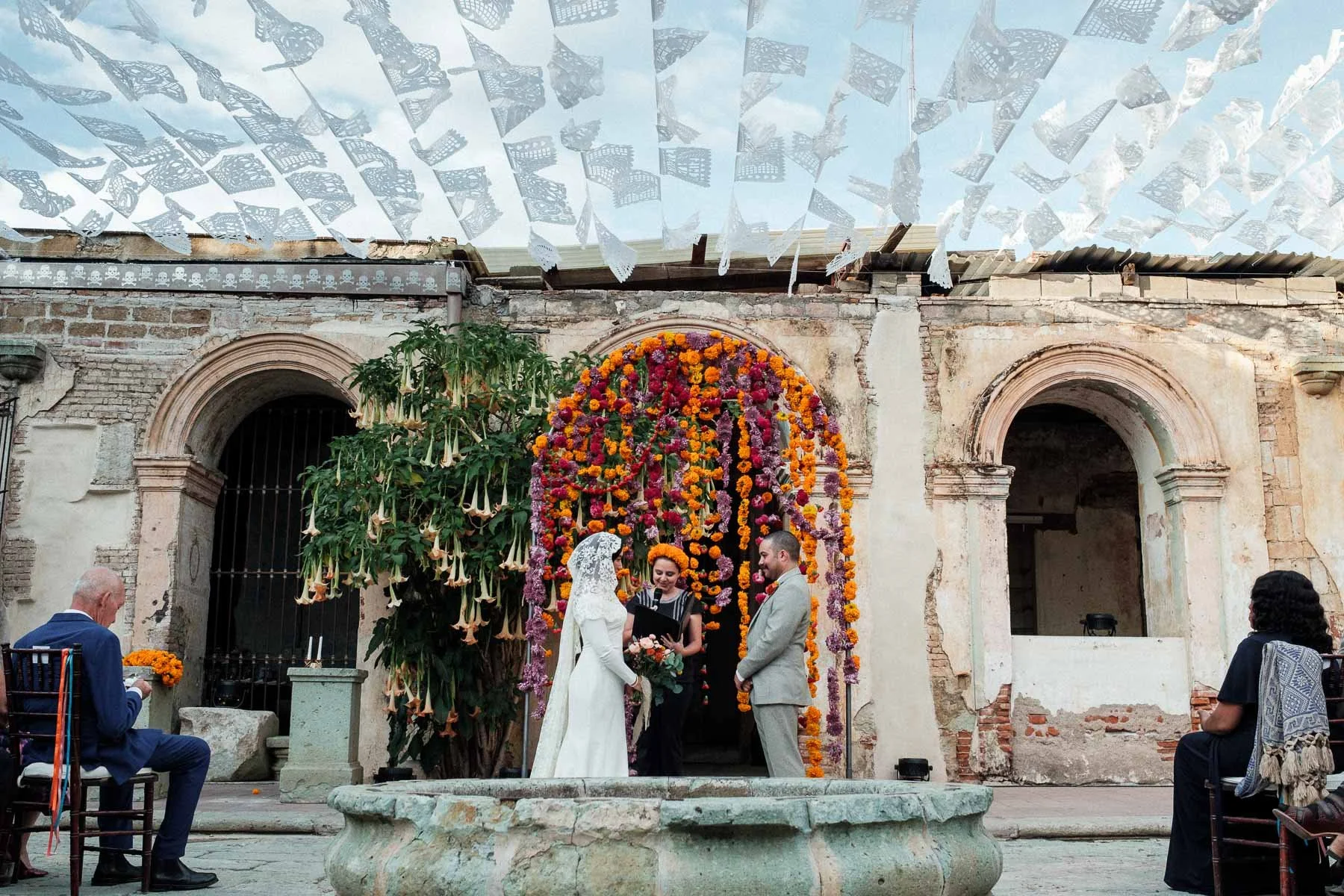 A beautiful wedding ceremony setup at Proyecto Murguía featuring traditional white papel picado and lush floral arrangements against the historic ruins.