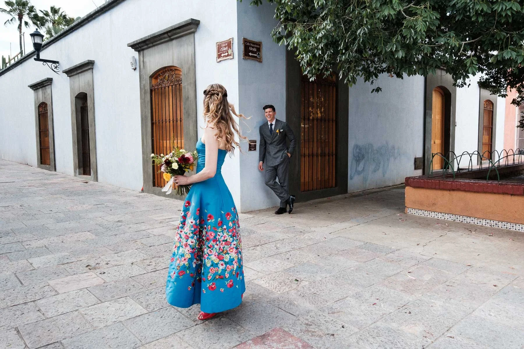 An unscripted moment of the bride glancing at the groom against the deep blue walls of Oaxaca’s city center.
