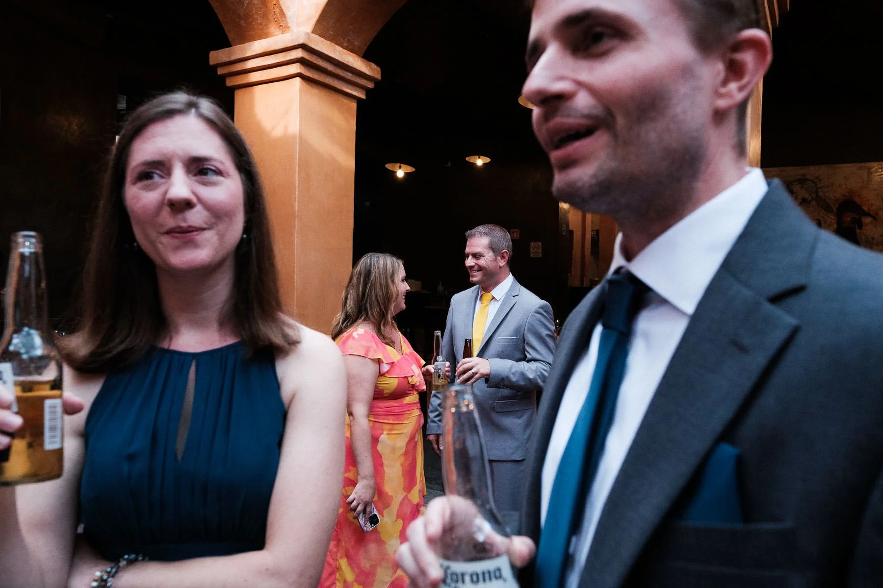 A street photography style shot of wedding guests with beers, naturally framing another couple in the background.