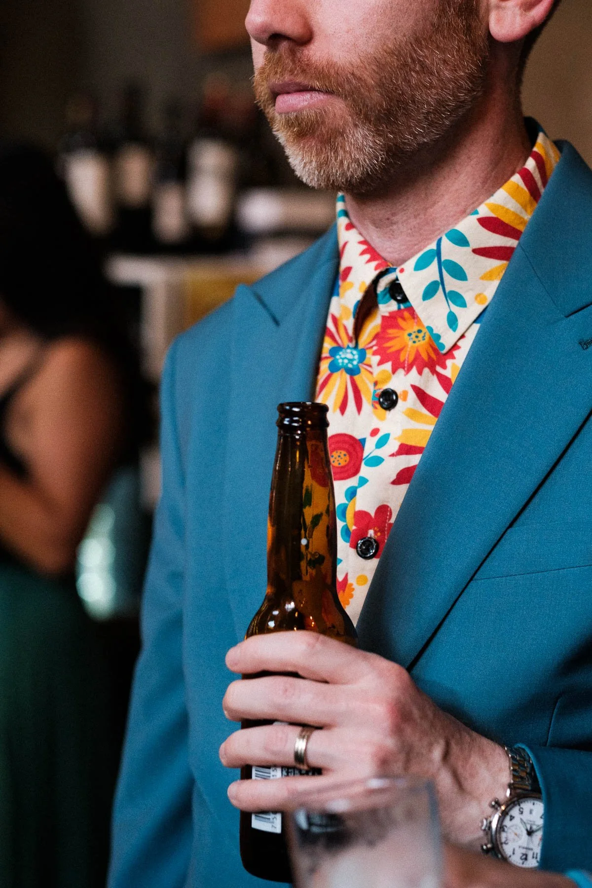 A guest in a colorful shirt and blue suit enjoying a beer at a wedding in the heart of Oaxaca.