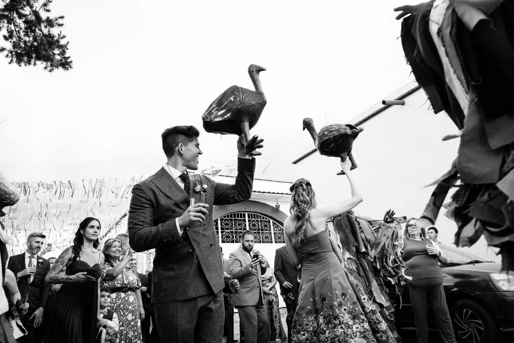 The couple laughing and holding traditional papier-mâché "guajolotes" during their wedding celebration.