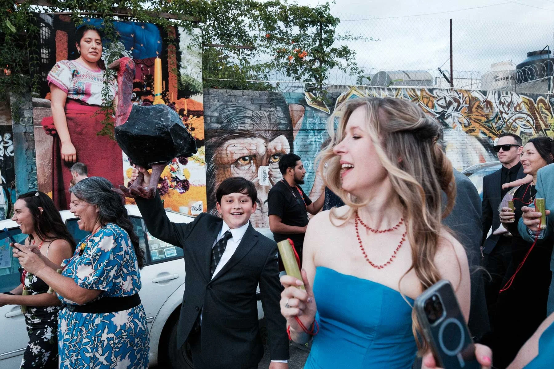 A layered shot featuring a child with a guajolote, the bride in the foreground, and Oaxacan murals.