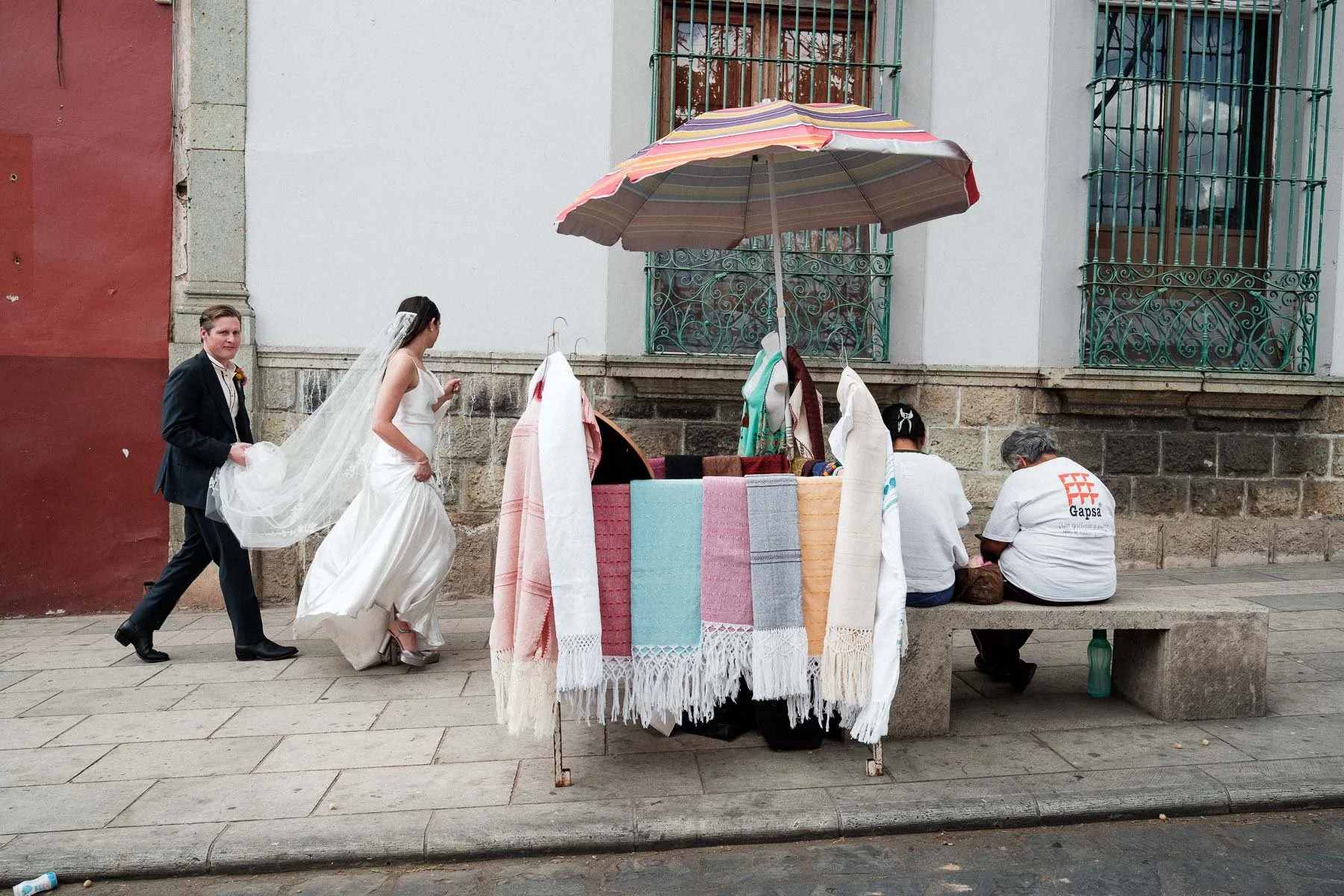 Newlyweds walking past a traditional local craft stand during a documentary session in Oaxaca.