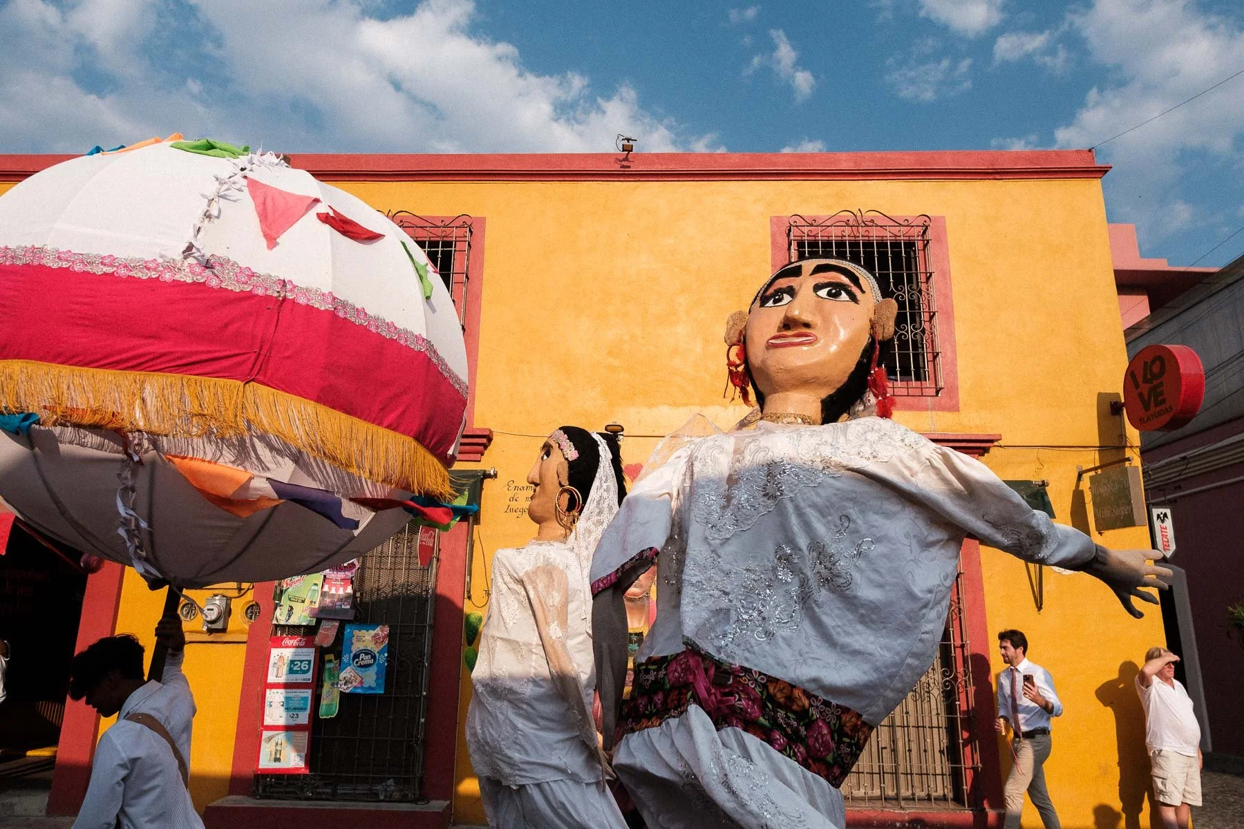 Iconic giant Calenda puppets set against the bright Oaxaca sun and blue sky.