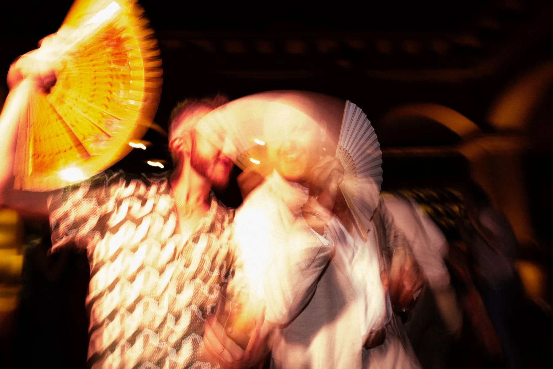 A creative long-exposure shot of guests dancing with hand fans.