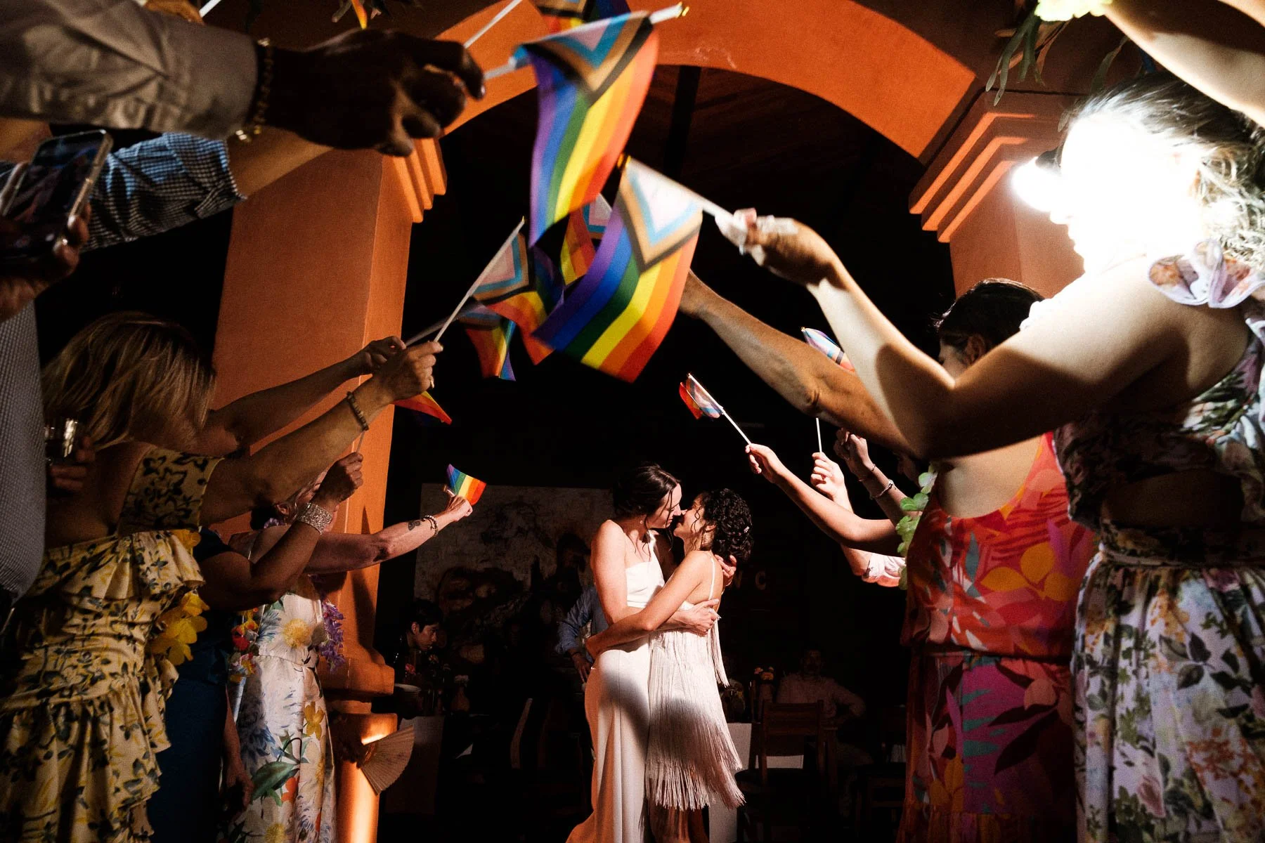 A final, beautiful kiss between the brides surrounded by LGBTQ flags.