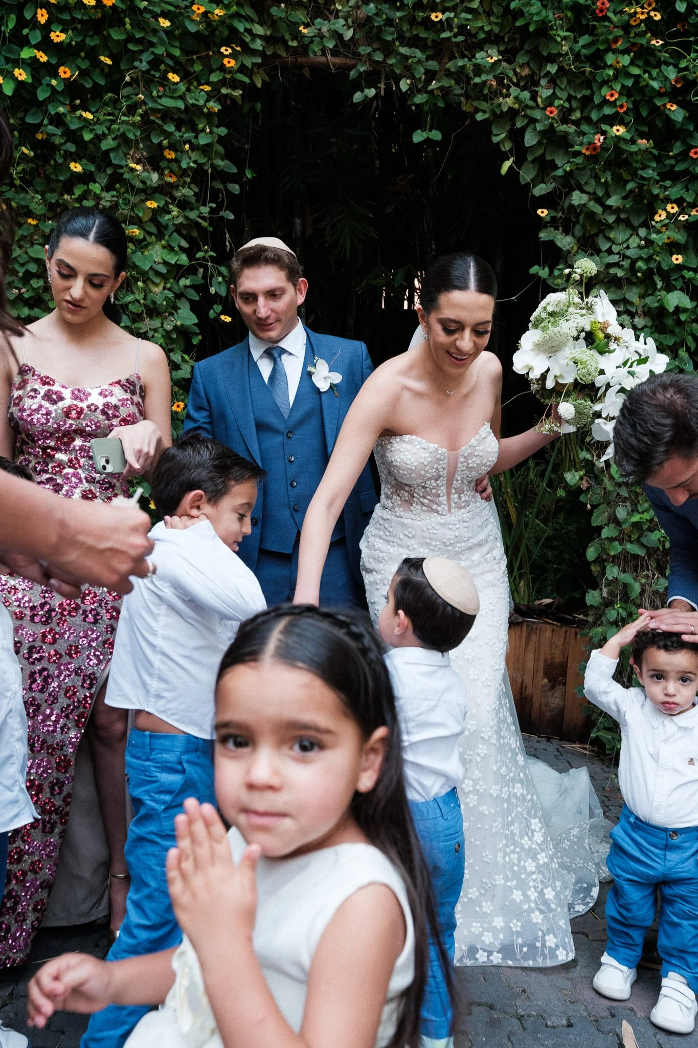 Documentary wedding photography in Mexico City: A bride and groom attempt to organize children for a group photo during a Jewish wedding celebration, capturing a layered and unscripted moment of chaos and real interaction.