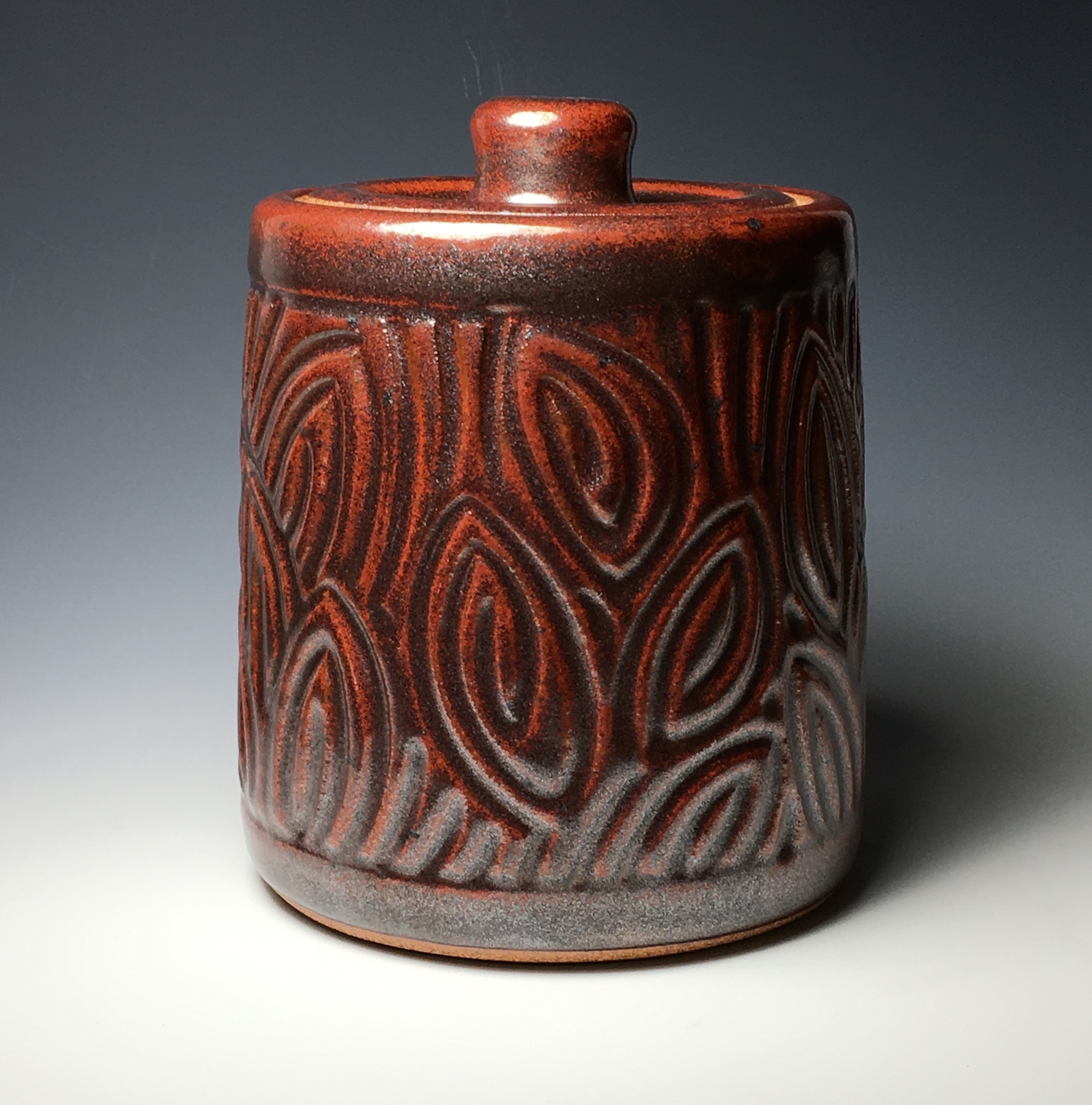 Kitchen storage canister. Approximately eight inches tall and six inches wide. "Ojata" red glaze with incised leaf motif.