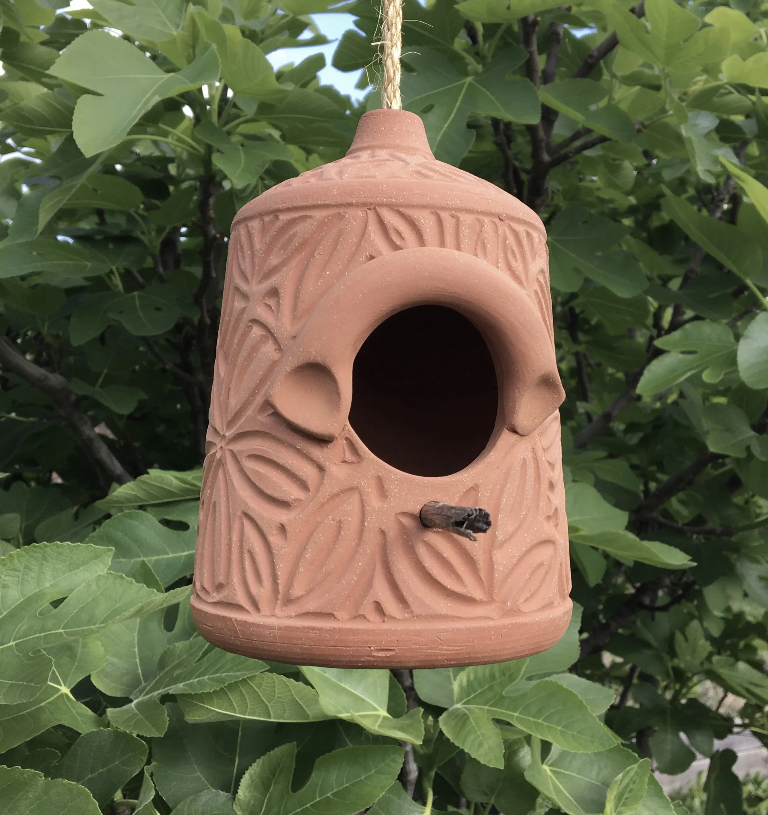 Terra cotta birdhouse with leaf design carved freehand. measures approximately nine inches tall with a six inch diameter.