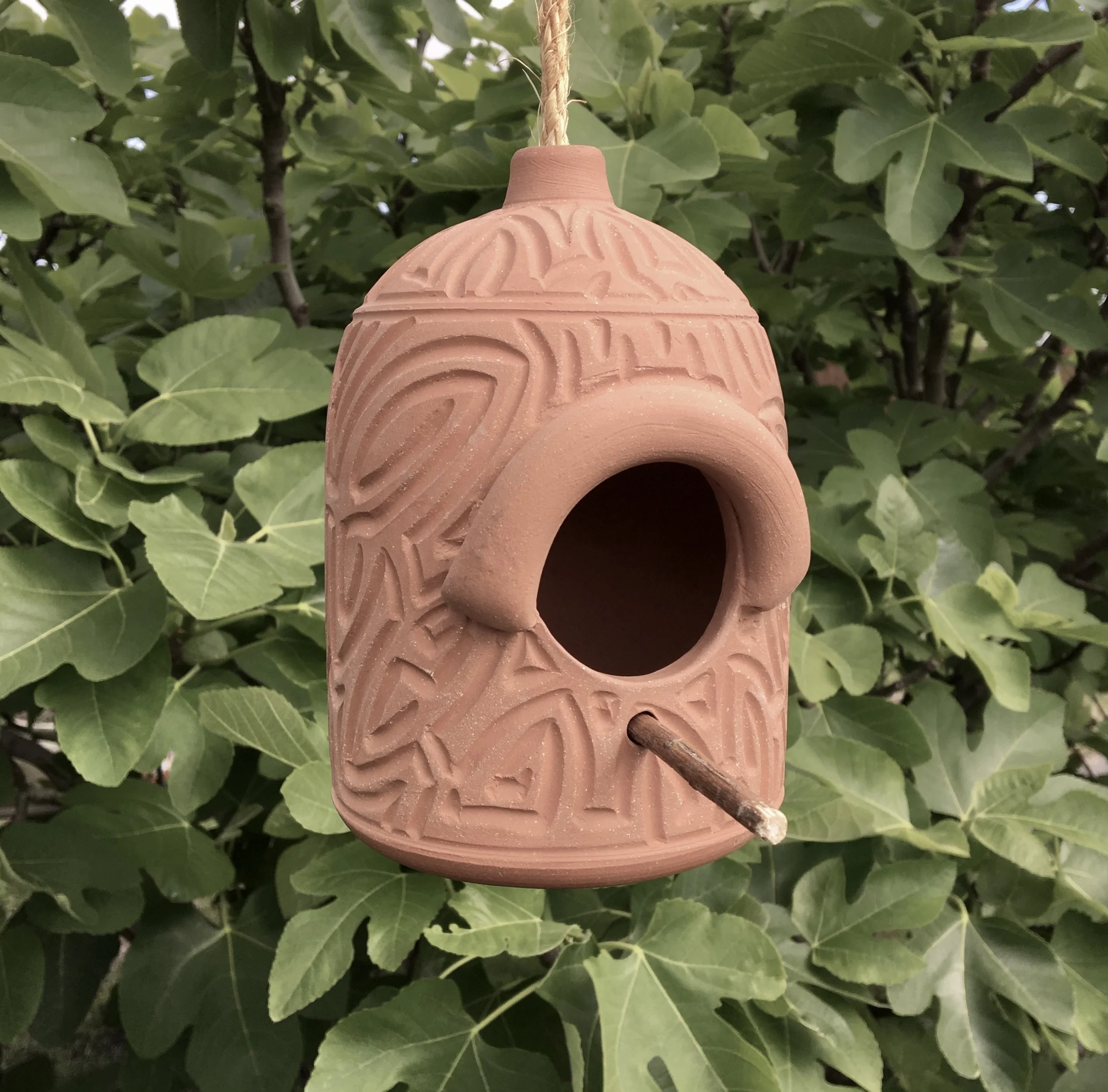 Terra cotta bird house with archway pattern carved freehand. Measures approximately eight inches tall with a five inch diameter.