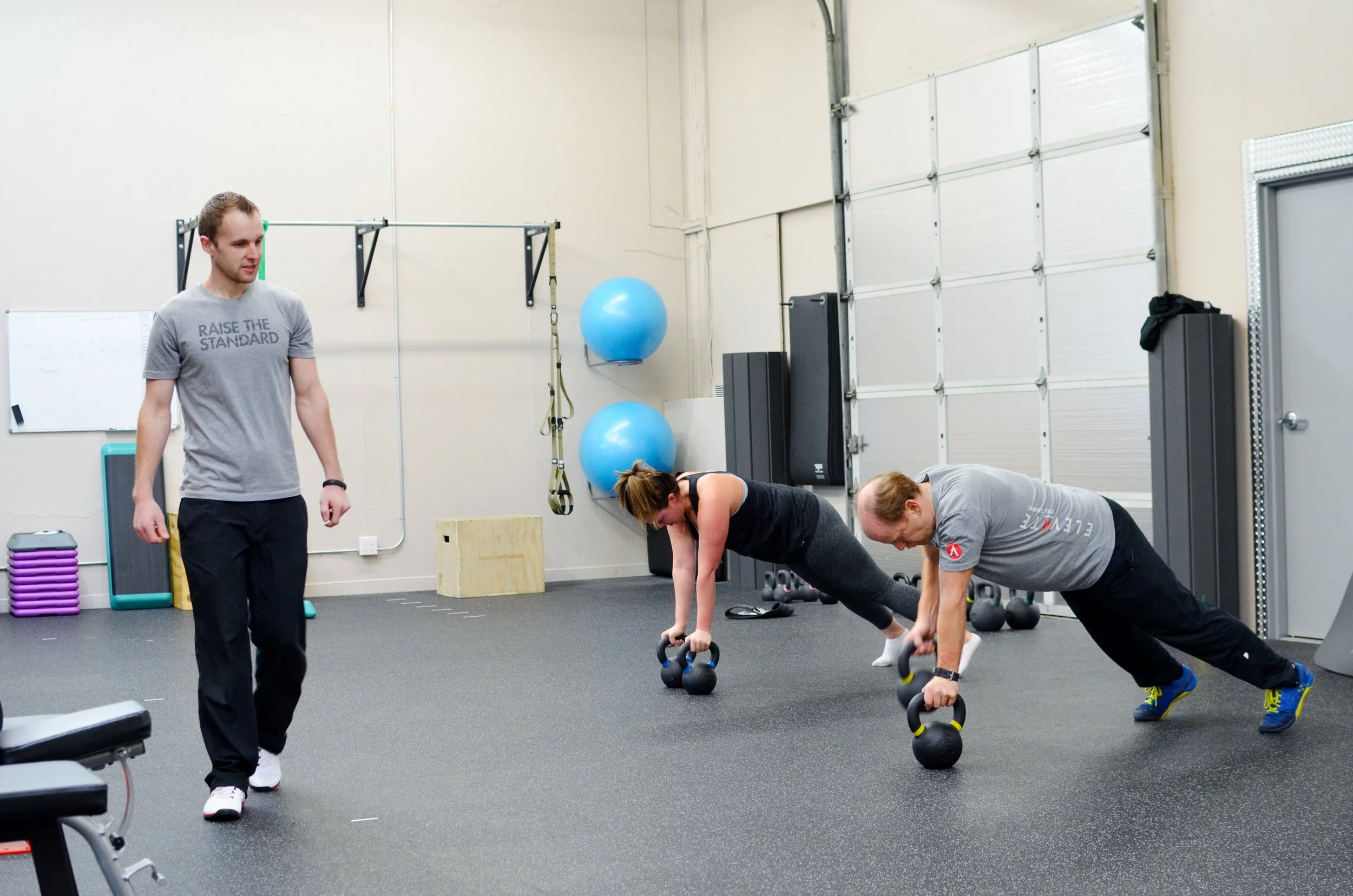 A coach supervises two clients training with kettlebells at Elevate Health & Performance.