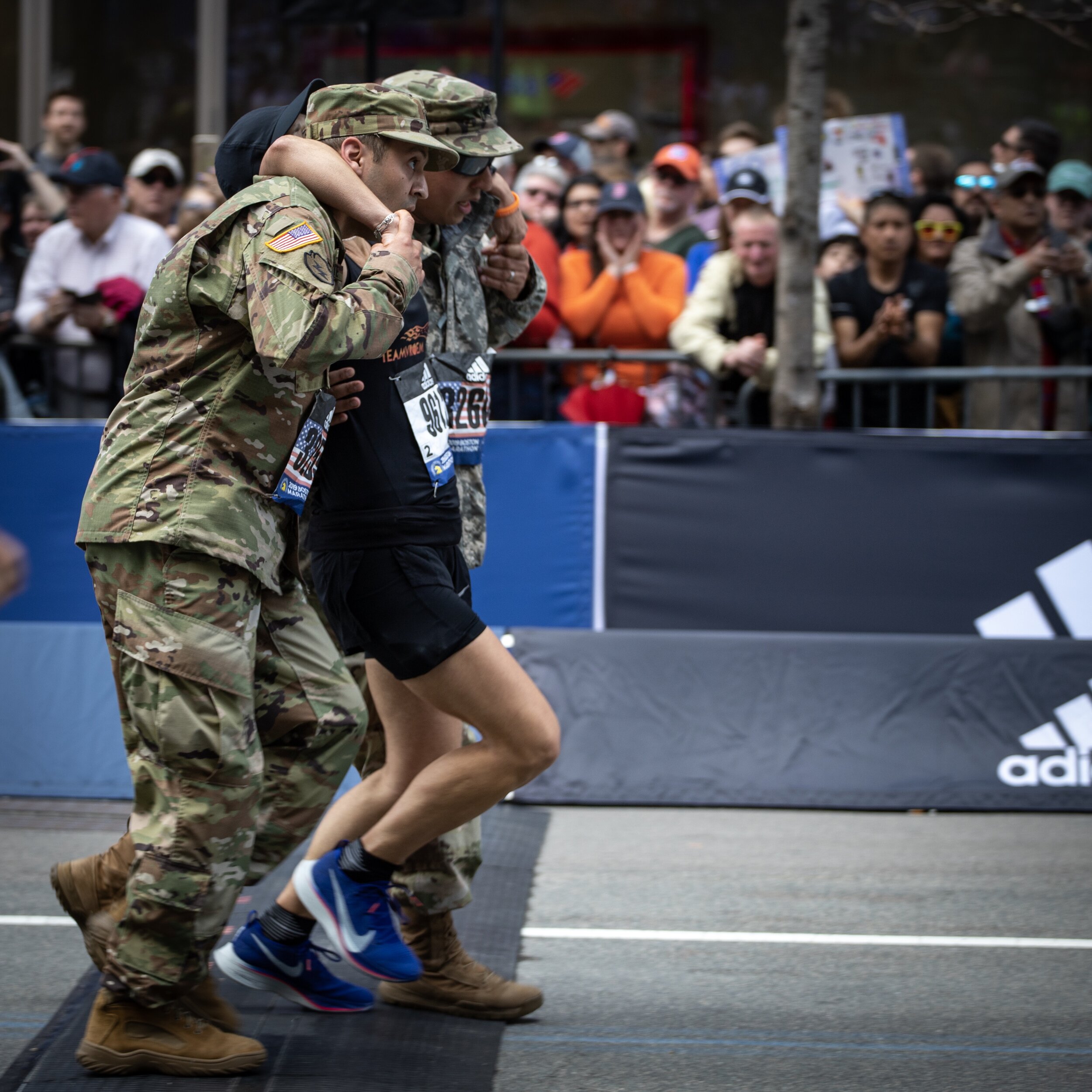 Military members help a runner cross the Boston Marathon finish line, 2019