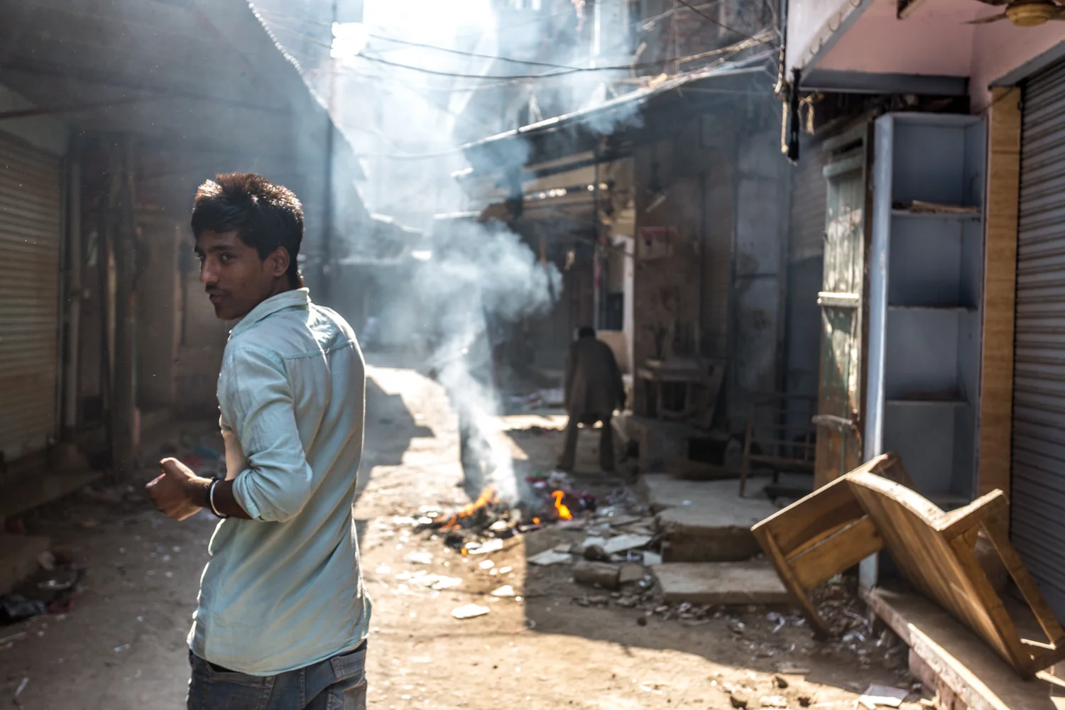 Surrounding the Harmandir Sahib complex is gritty capillary network of narrow market streets. In this picture,&nbsp;a young man walks past burning trash on a Monday, the day of the week when many stores close.&nbsp;