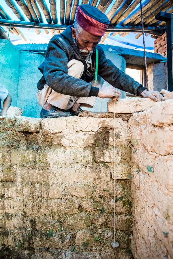 A mason using a plumb bob to check the vertical alignment of an adobe wall. 