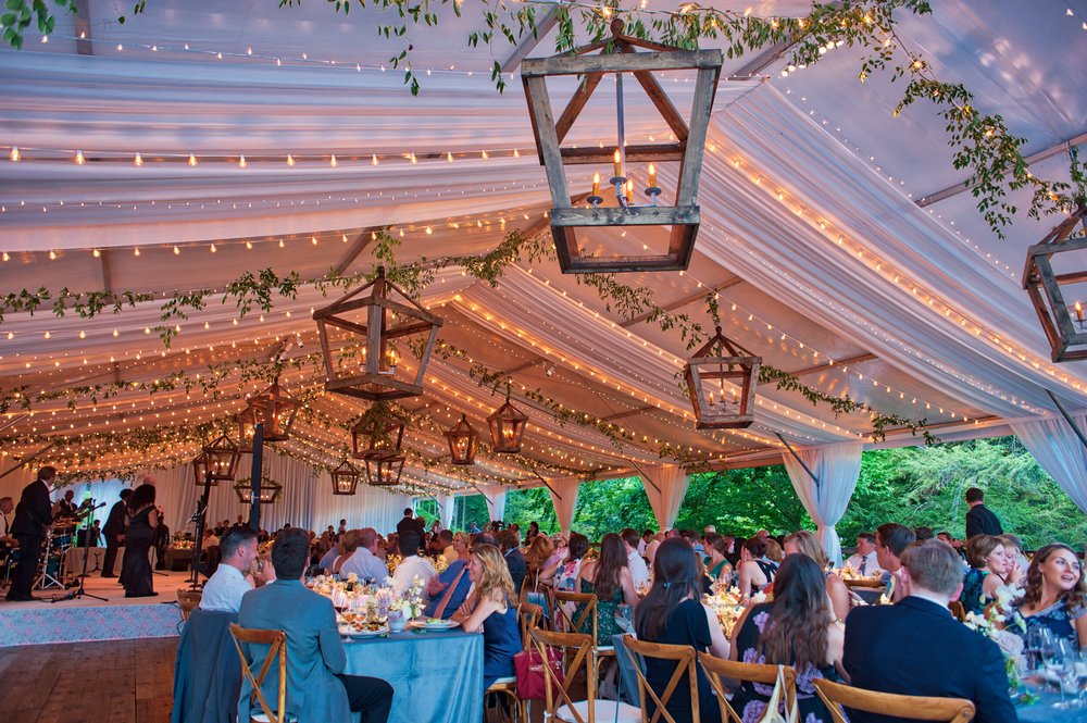 Draped tent ceiling with lanterns and string lights over a seated dinner