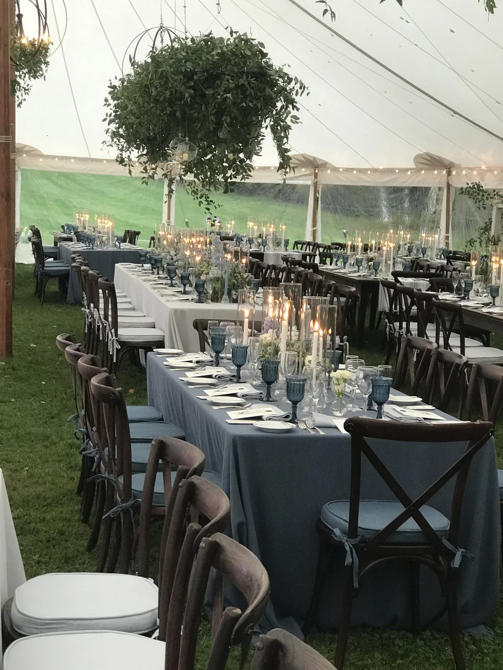 Elegant banquet tables with blue linens, candles, floral centerpieces, and hanging greenery inside a tent at Edson Hill Inn, installed by Rain or Shine Tent and Events