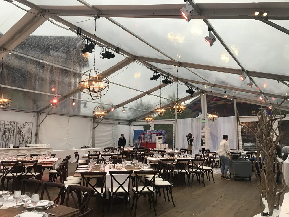 Clear-top event tent with banquet tables, chandeliers, 4-Wall lighting, and wood flooring at The Lodge at Spruce Peak, installed by Rain or Shine Tent and Events