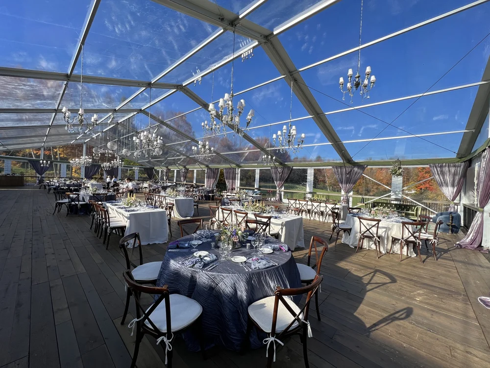 Clear-top event tent with banquet tables, chandeliers, and wood flooring, installed by Rain or Shine Tent and Events