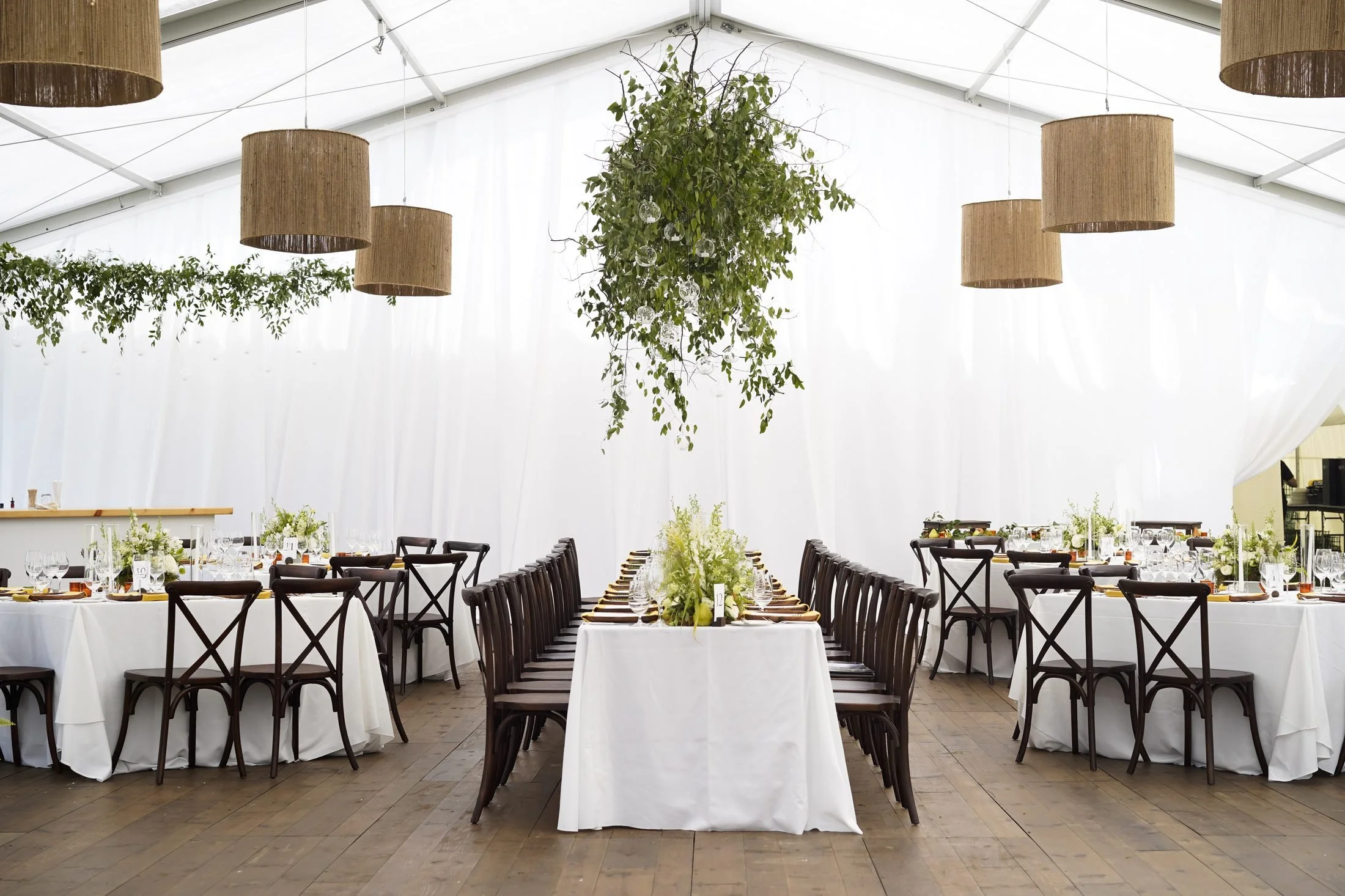 Draped white tent interior with New England plank flooring, cross-back chairs, suspended greenery and pendant lighting at a Woodstock, Vermont wedding by Rain or Shine Tent and Events