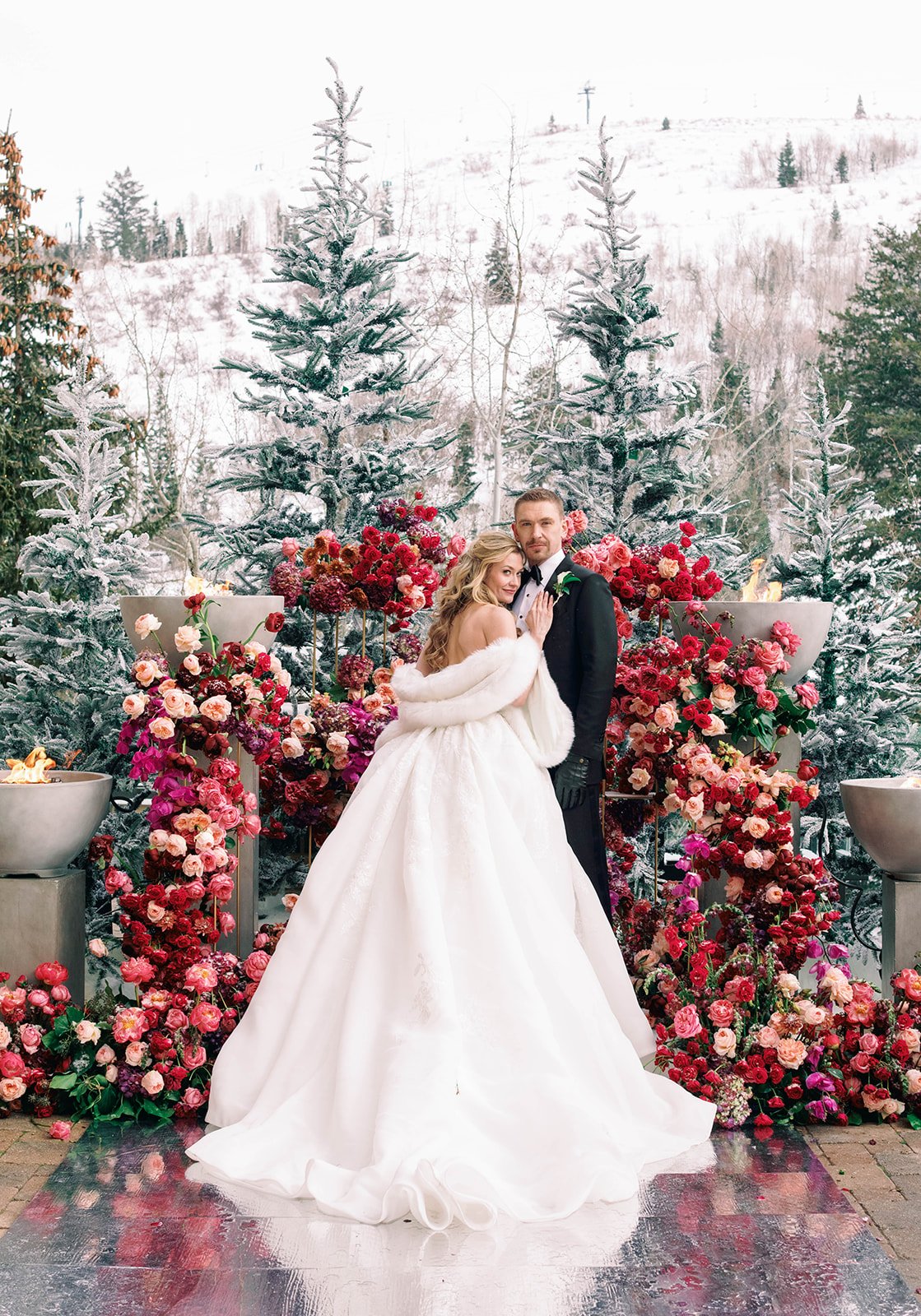 Winter ceremony on the Astor Terrace at St. Regis Deer Valley featuring Catherine and Mitchell surrounded by lush pink and red florals, snow-covered evergreens, and a romantic alpine backdrop, designed and planned by Michelle Leo Events.