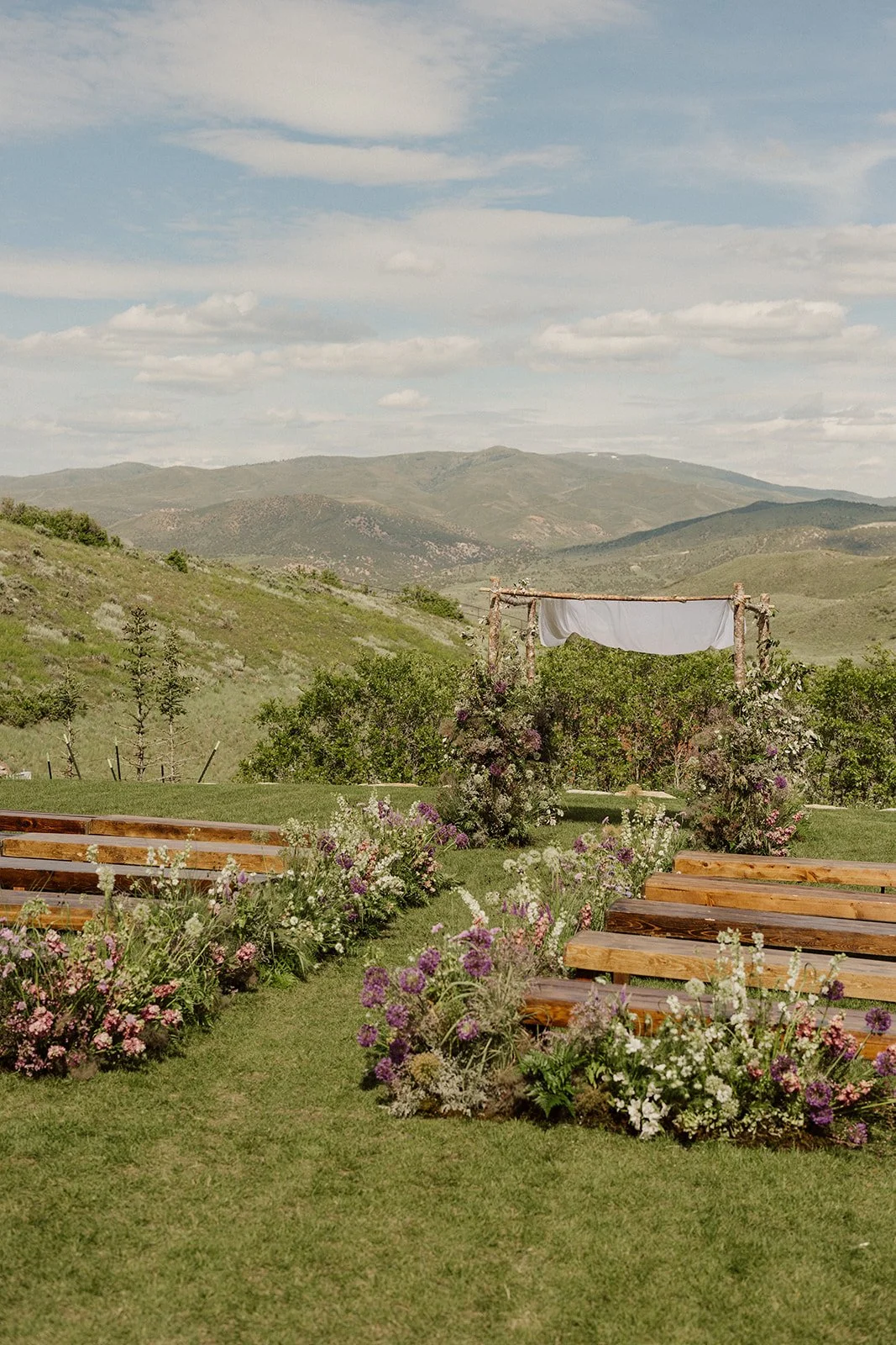 Outdoor wedding ceremony setup on the Arena Lawn at The Lodge at Blue Sky Auberge with wooden benches, meadow-style florals, and sweeping mountain views, planned and designed by Michelle Leo Events.