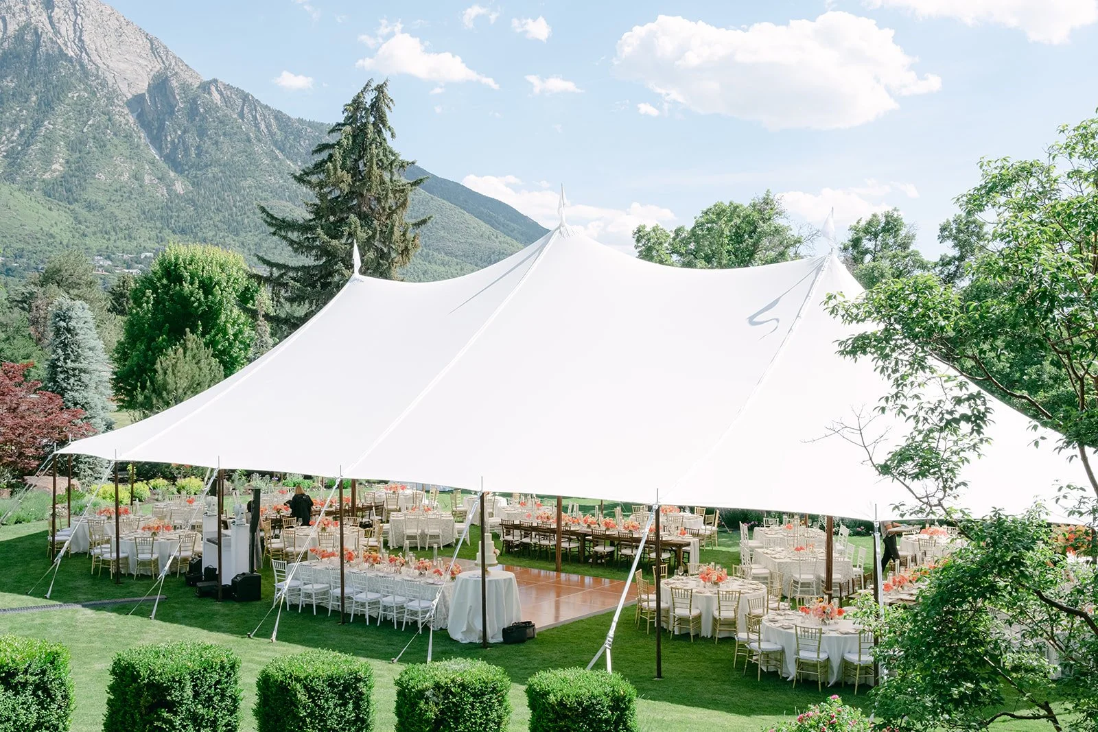 Elegant white sailcloth wedding tent set on a private Utah estate, featuring outdoor reception tables, a wooden dance floor, and scenic mountain views.