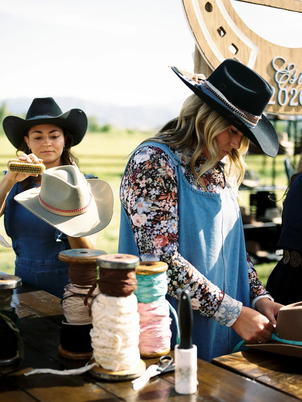 Guests personalize cowboy hats with custom trims, ribbons, and embellishments at an interactive hat bar during a Western-chic wedding welcome party at River Bottoms Ranch in Utah. This unique guest experience was part of a luxury destination wedding 