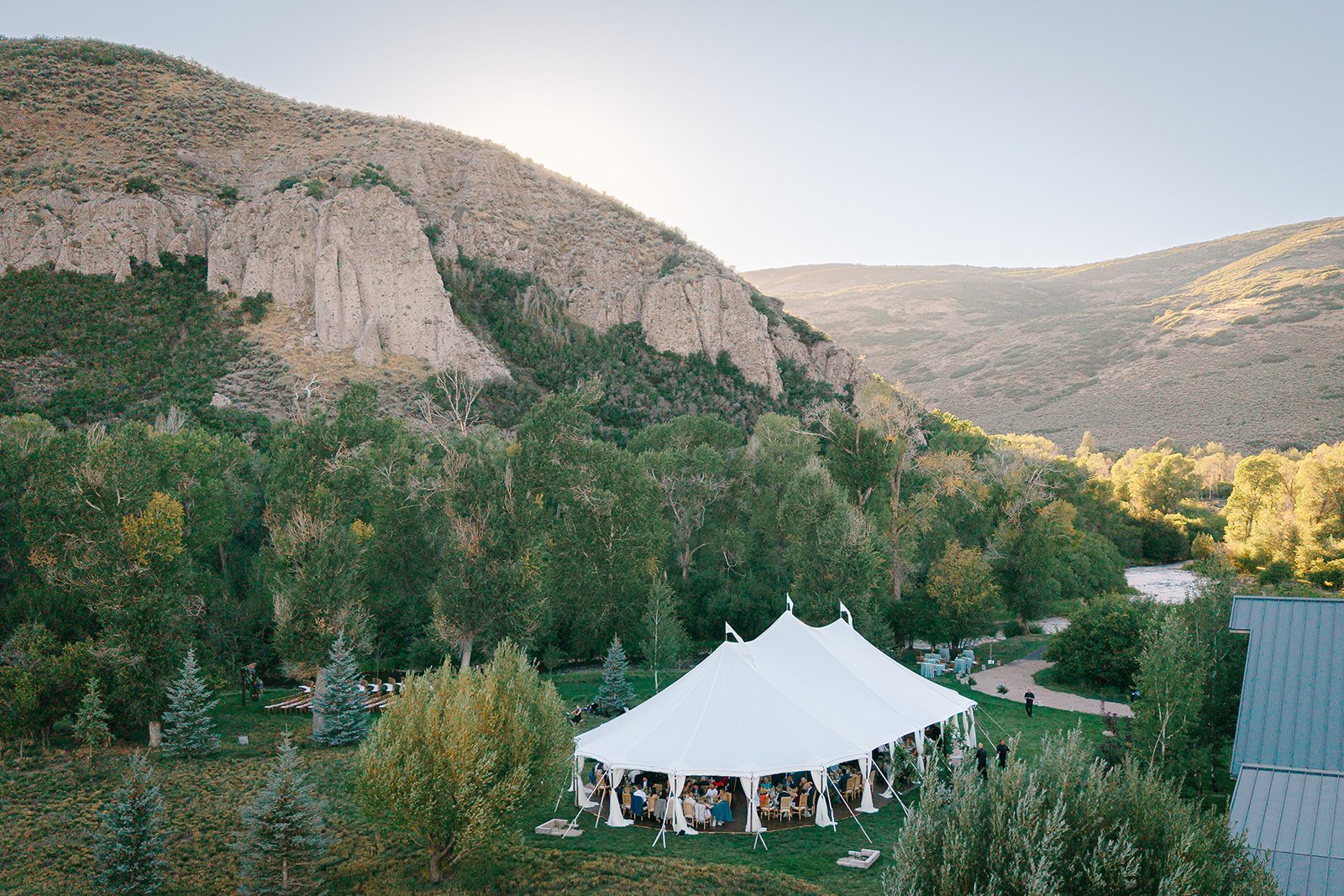 Aerial view of an elegant white wedding reception tent nestled among trees and mountains at 4U Ranch in Utah, showcasing an outdoor destination wedding planned by Michelle Leo Events.