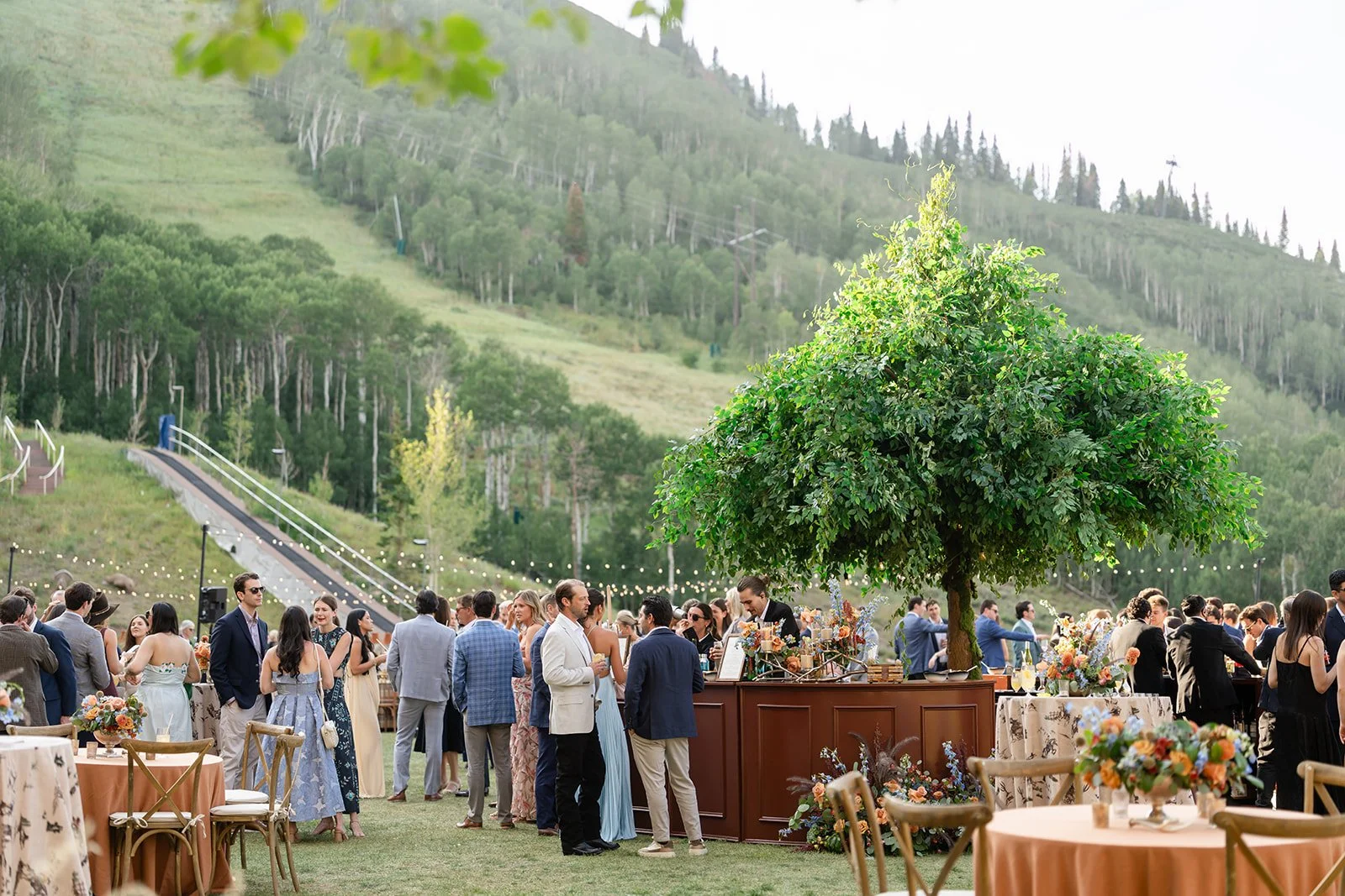Wedding guests gathering around a statement bar during an outdoor mountain reception