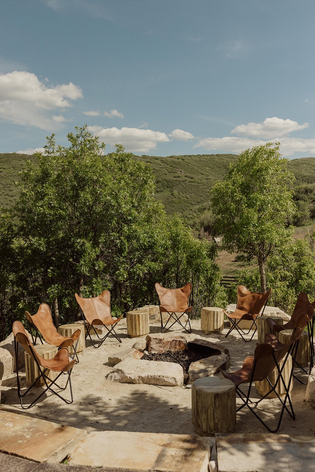 Leather lounge chairs arranged around a stone fire pit on the Arena Patio at The Lodge at Blue Sky Auberge, set against a mountain landscape and designed for an outdoor gathering by Michelle Leo Events.