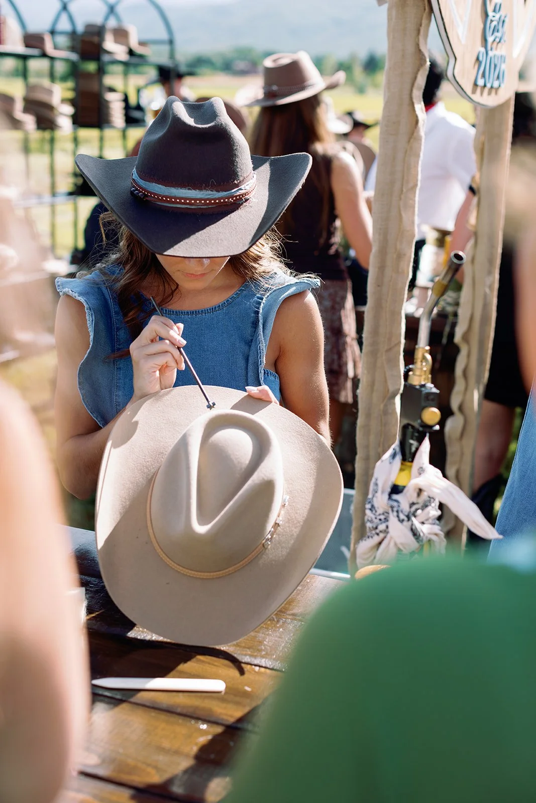 A wedding guest personalizes her cowboy hat with custom embellishments at an interactive hat-making station during a Western-chic welcome party at River Bottoms Ranch in Utah. This creative guest experience was part of a luxury destination wedding we