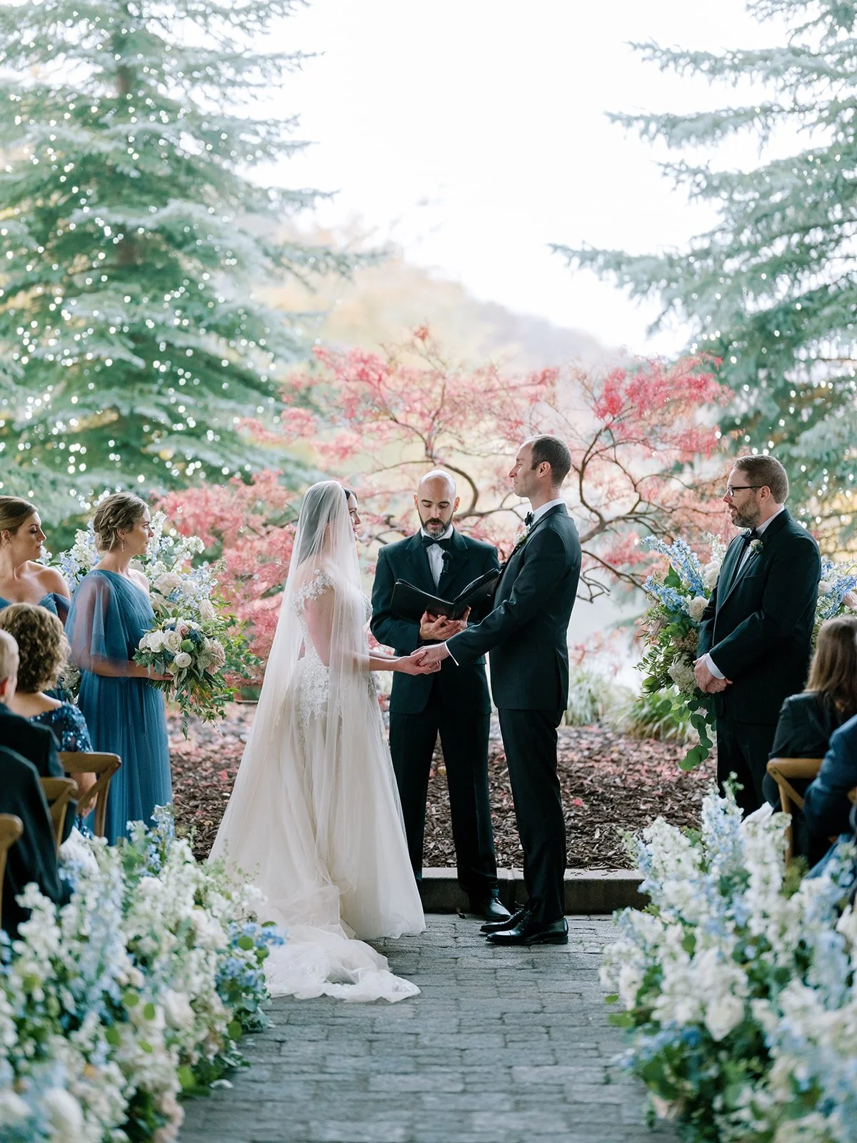 Wedding ceremony under the porticochere at St. Regis Deer Valley with bride and groom exchanging vows amid lush blue and white florals, framed by mountain greenery, planned and designed by Michelle Leo Events in Deer Valley, Utah.