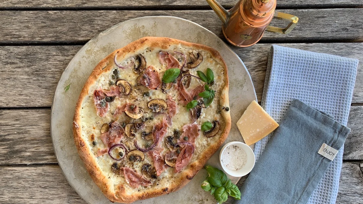 Server pizzaen med revet parmesan og frisk basilikum.