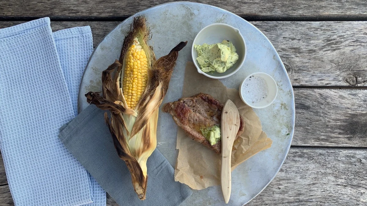 Ferdig grillede nakkekoteletter serveres med grillet mais og en raus skje med urtesmør.