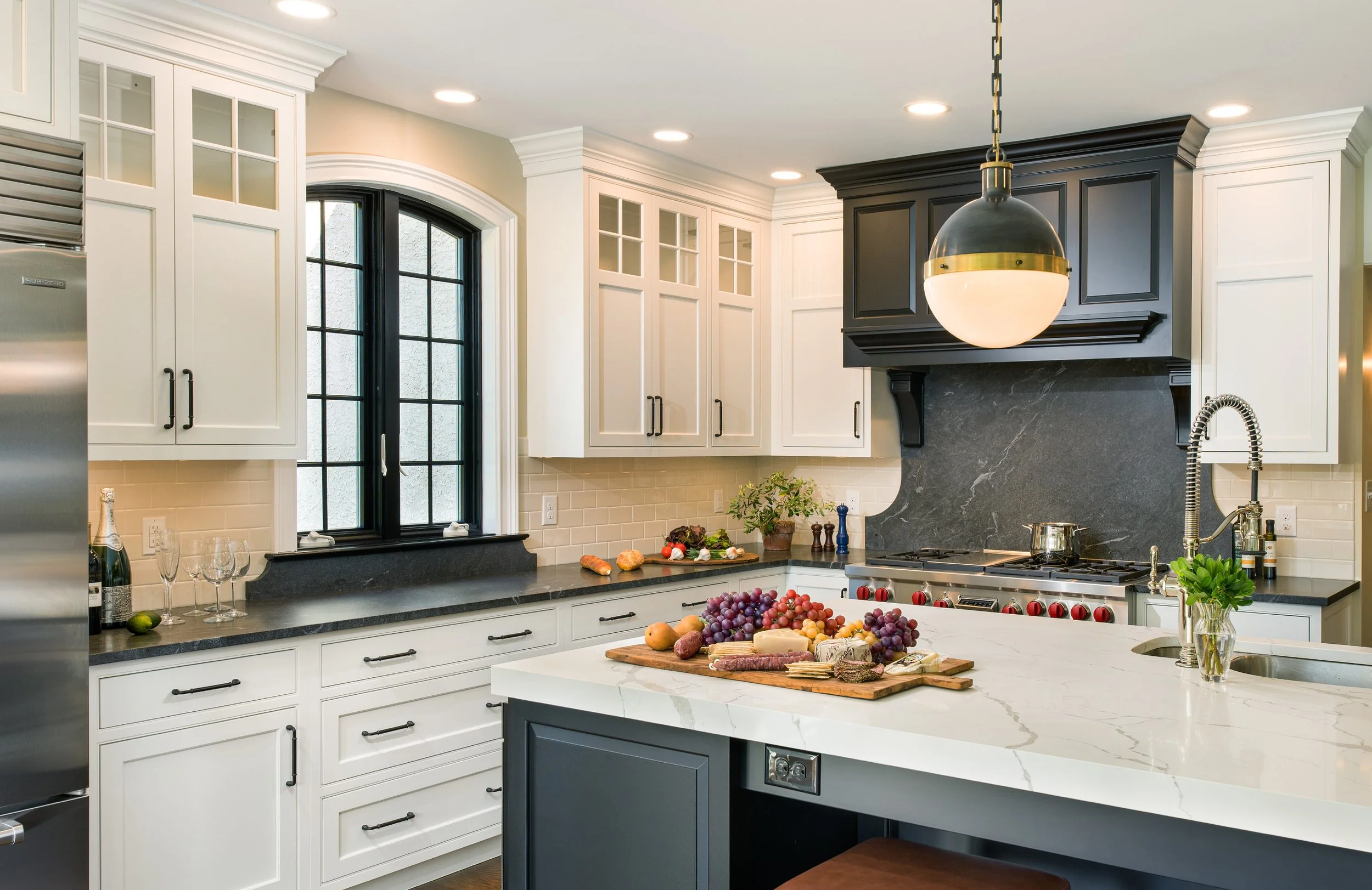 Modern kitchen with white cabinets, black accents, a window, and a black-and-white island topped with fruit and cheese.