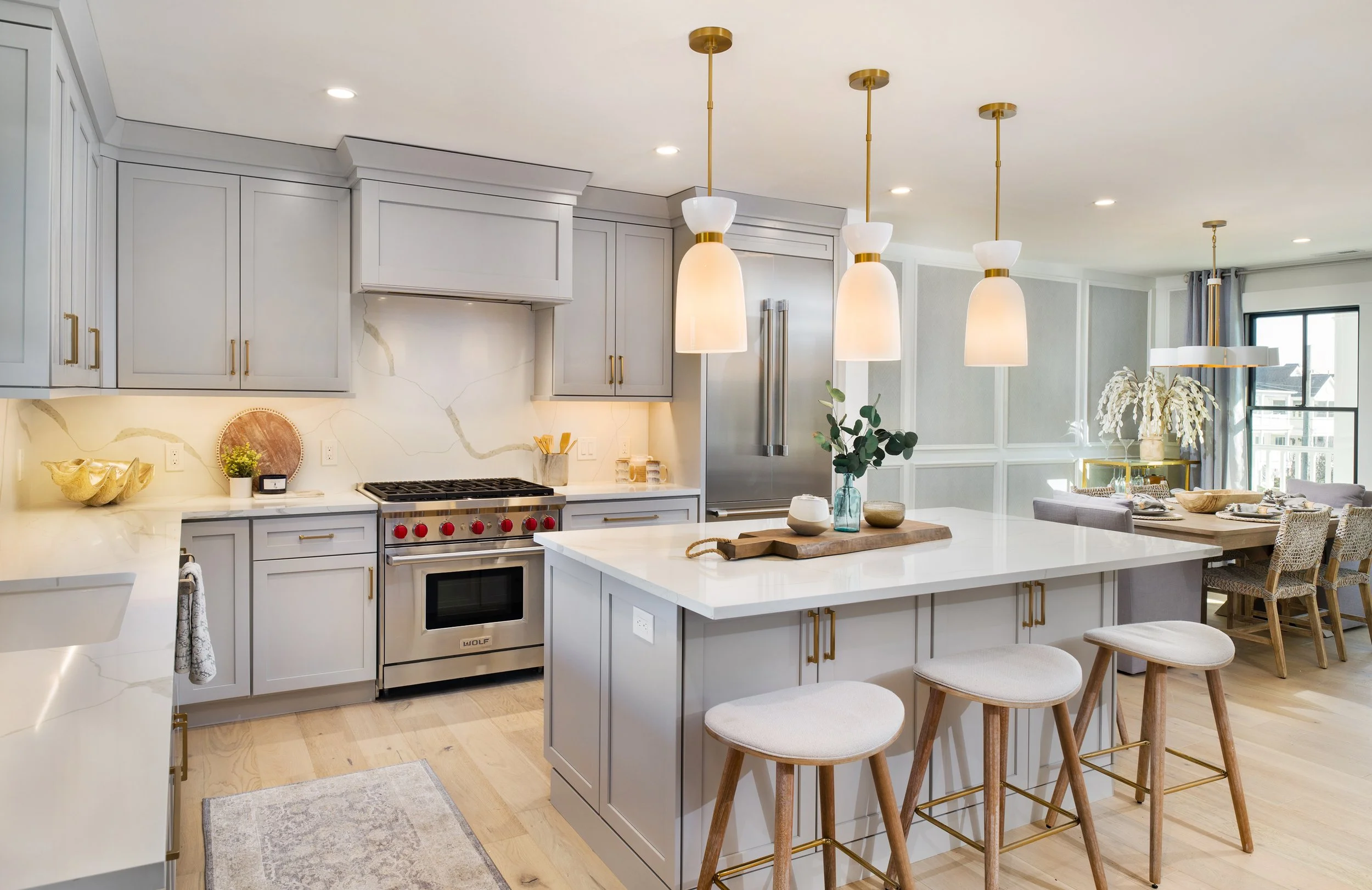 Modern kitchen with white cabinets, a kitchen island with stools, pendant lighting, and a dining area with a window view.