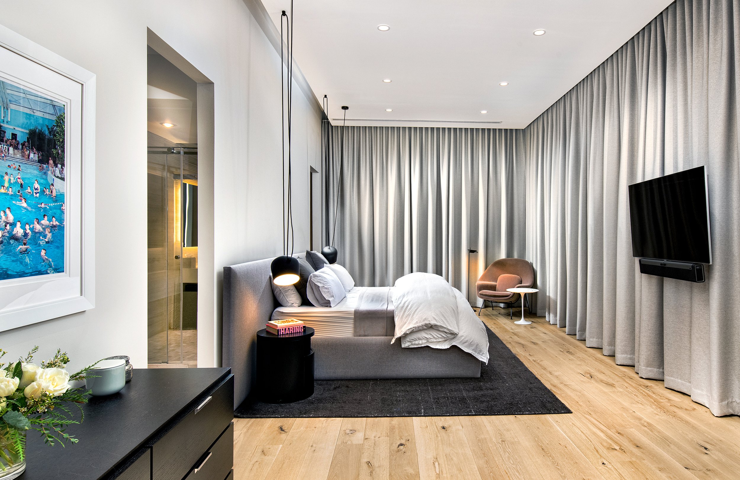 Modern hotel room with a bed, side table, chair, and flat-screen TV, with large curtains covering the window.