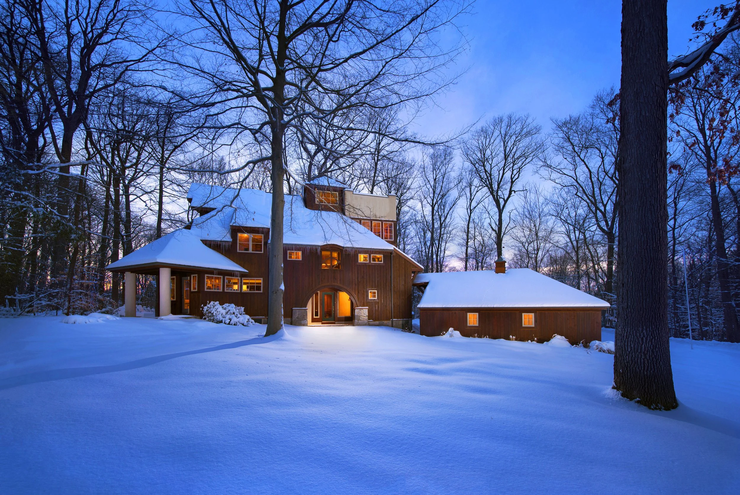 Twilight shot of a wood sided house surrounded by fluffy snow.