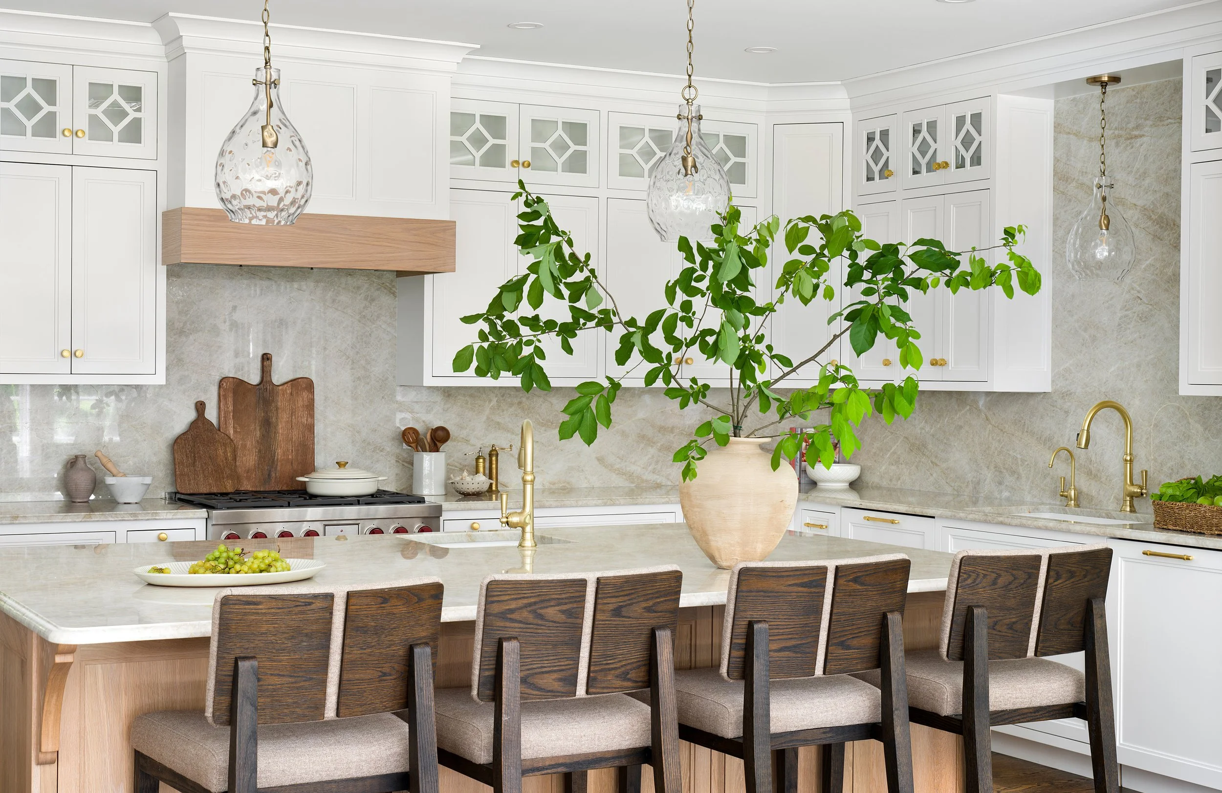 Modern kitchen with white cabinets, gold hardware, a large island with a beige countertop, and a potted plant with large green leaves.