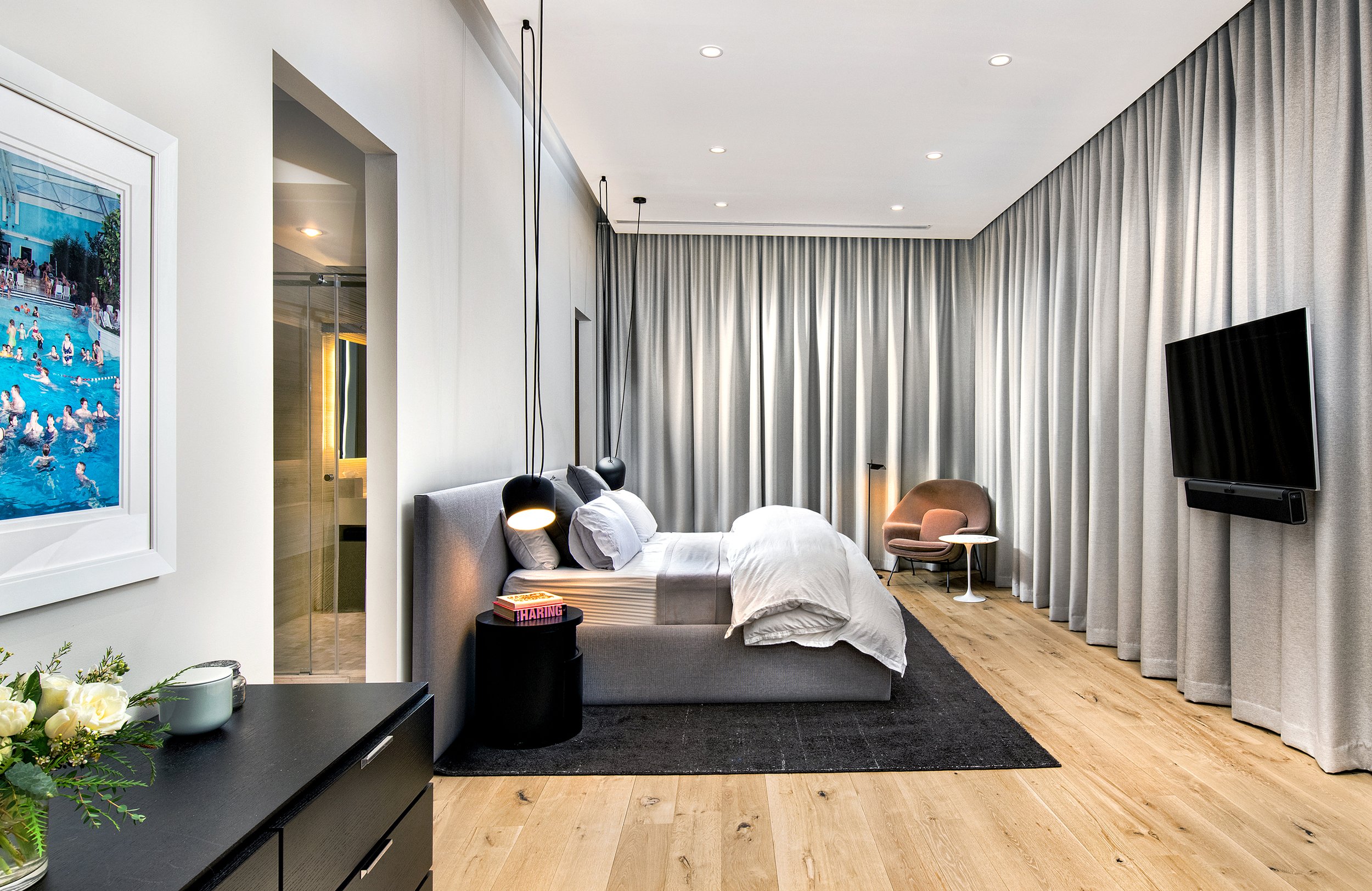 Modern bed, side table, chair, and flat-screen TV, with large curtains covering the window.