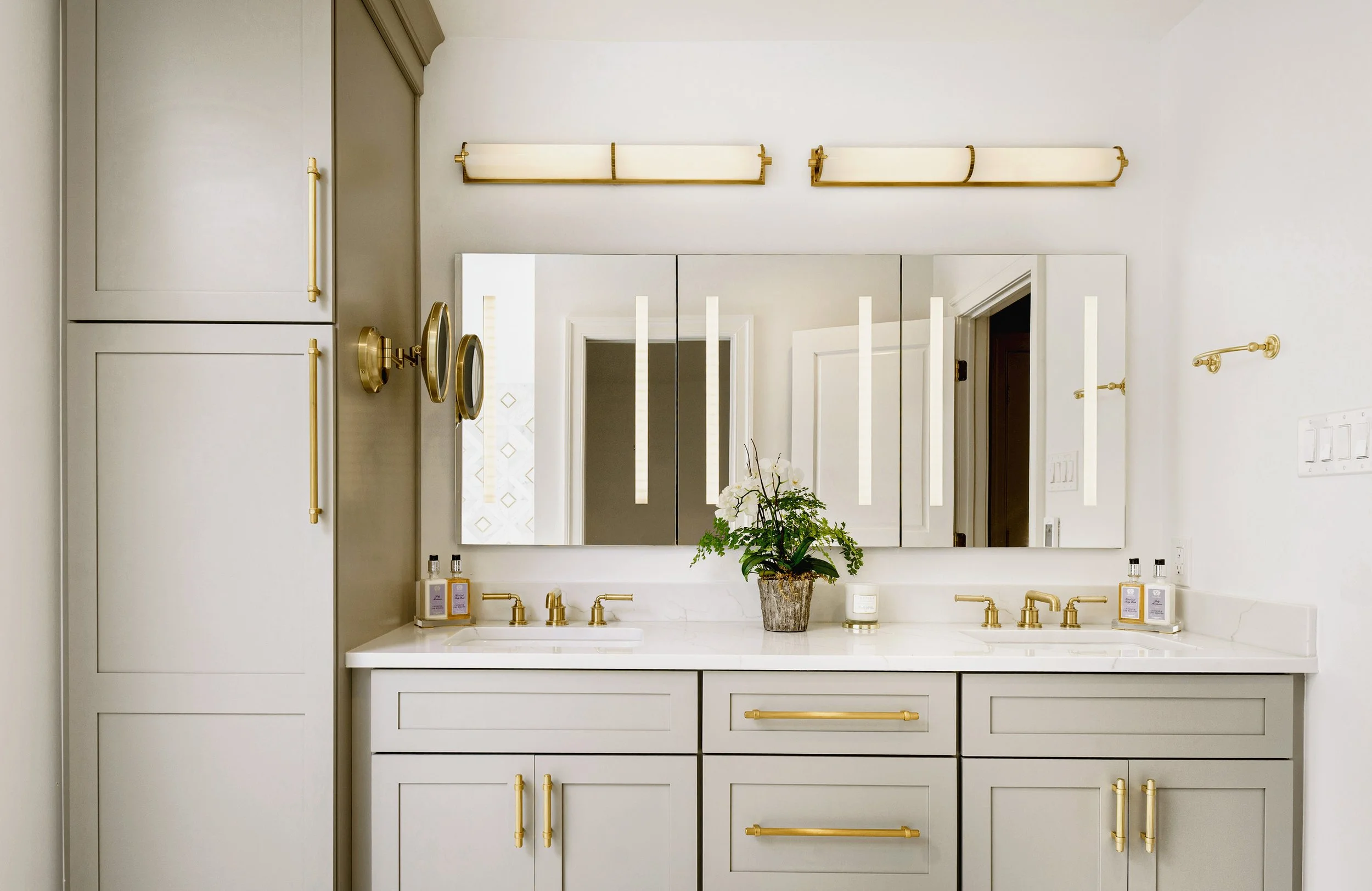 Bathroom vanity with a large mirror, gold fixtures, and a potted plant on the white countertop.