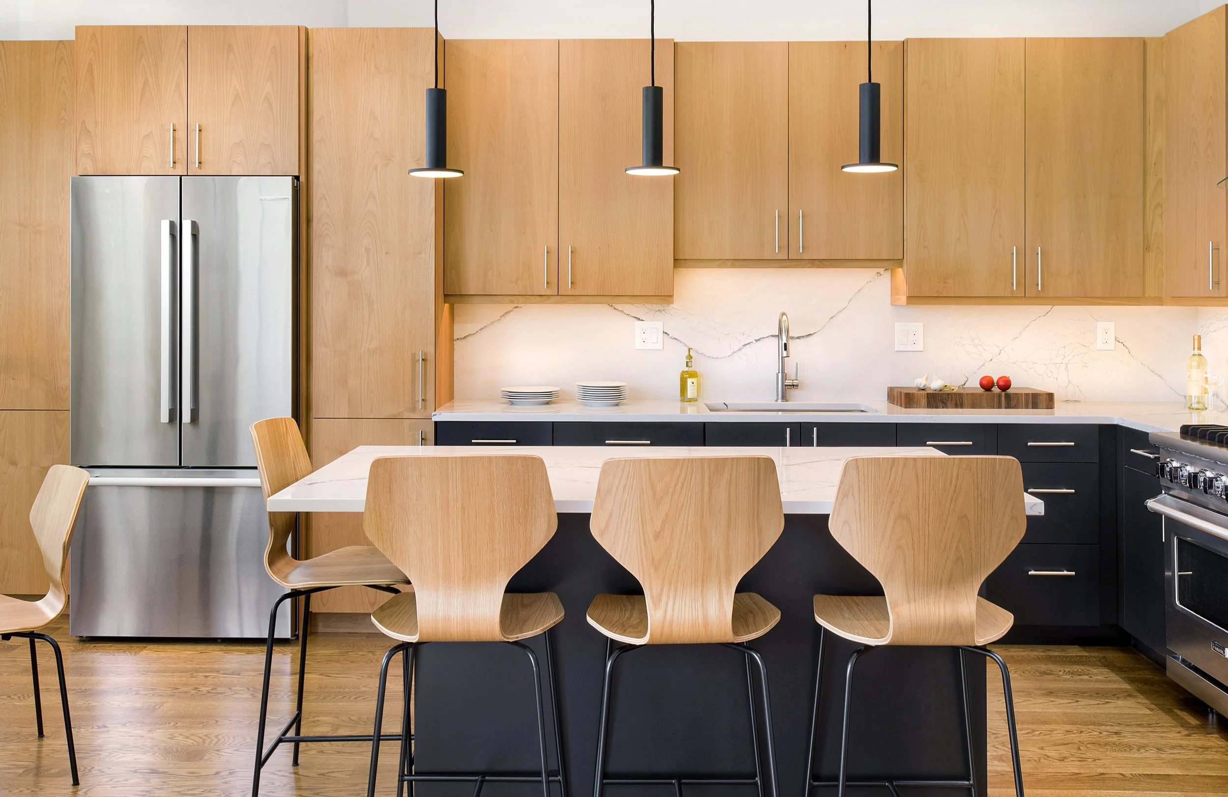 Modern kitchen with wooden cabinets, a marble backsplash, black pendant lighting, a stainless steel refrigerator, and a wooden dining table with matching chairs.